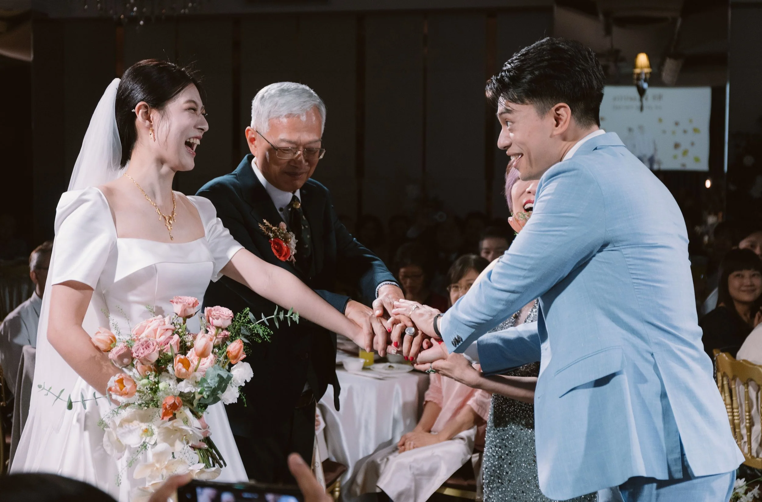 A bride and groom exchanging rings at their wedding ceremony, with an officiant present, during a celebration in a decorated venue.