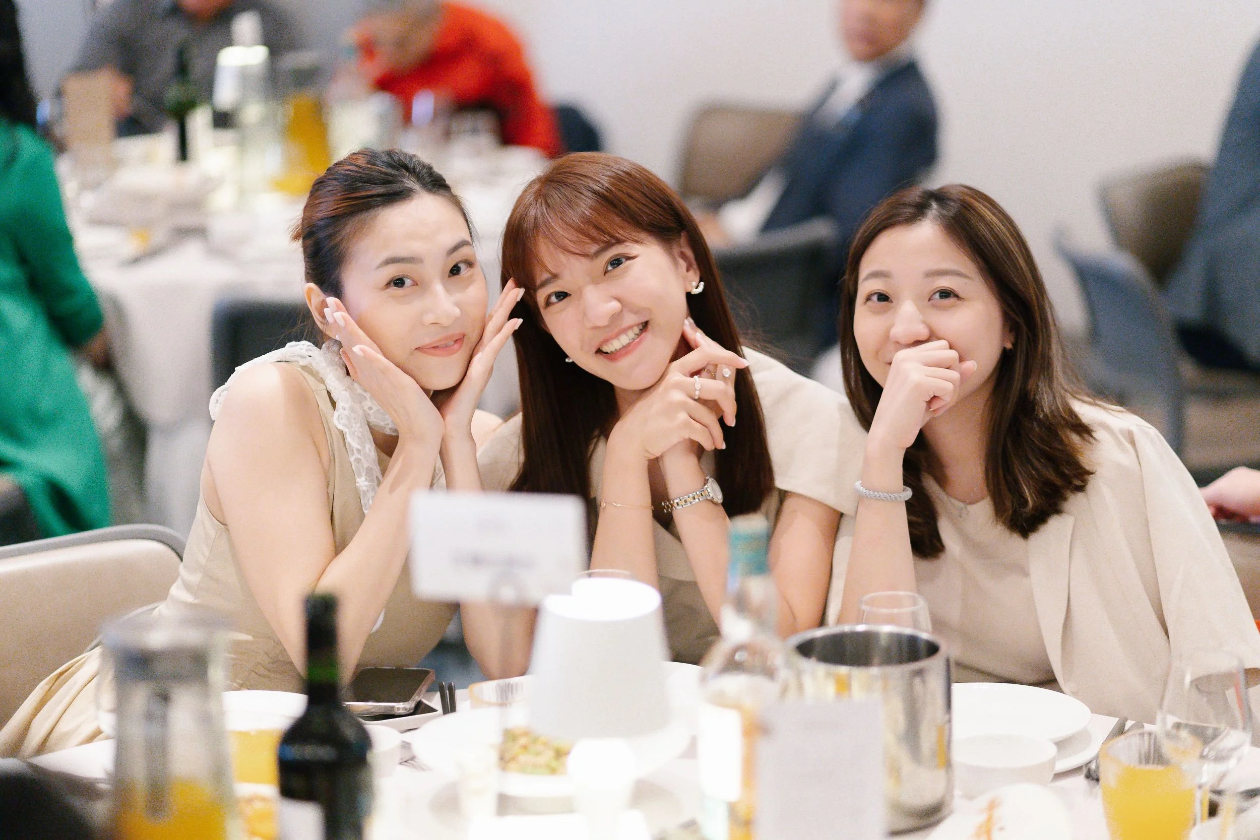 Three smiling women sitting at a round dinner table during a social gathering or celebration.