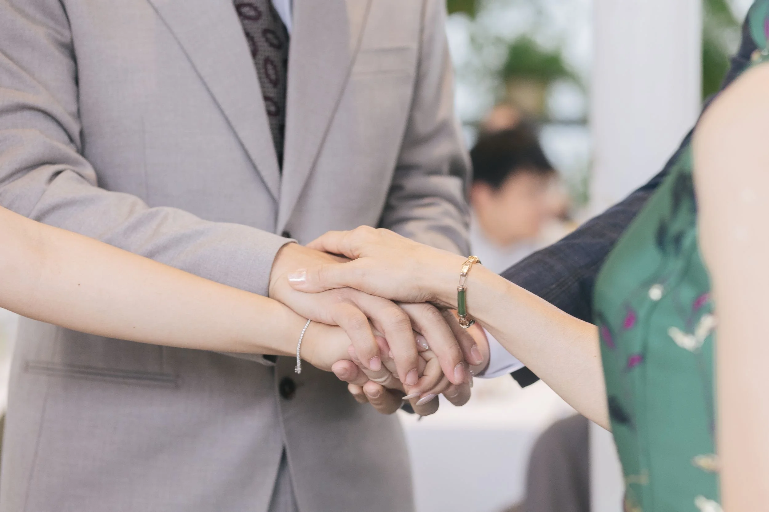 Two people shaking hands, one wearing a gray suit and the other wearing a green dress with floral pattern.