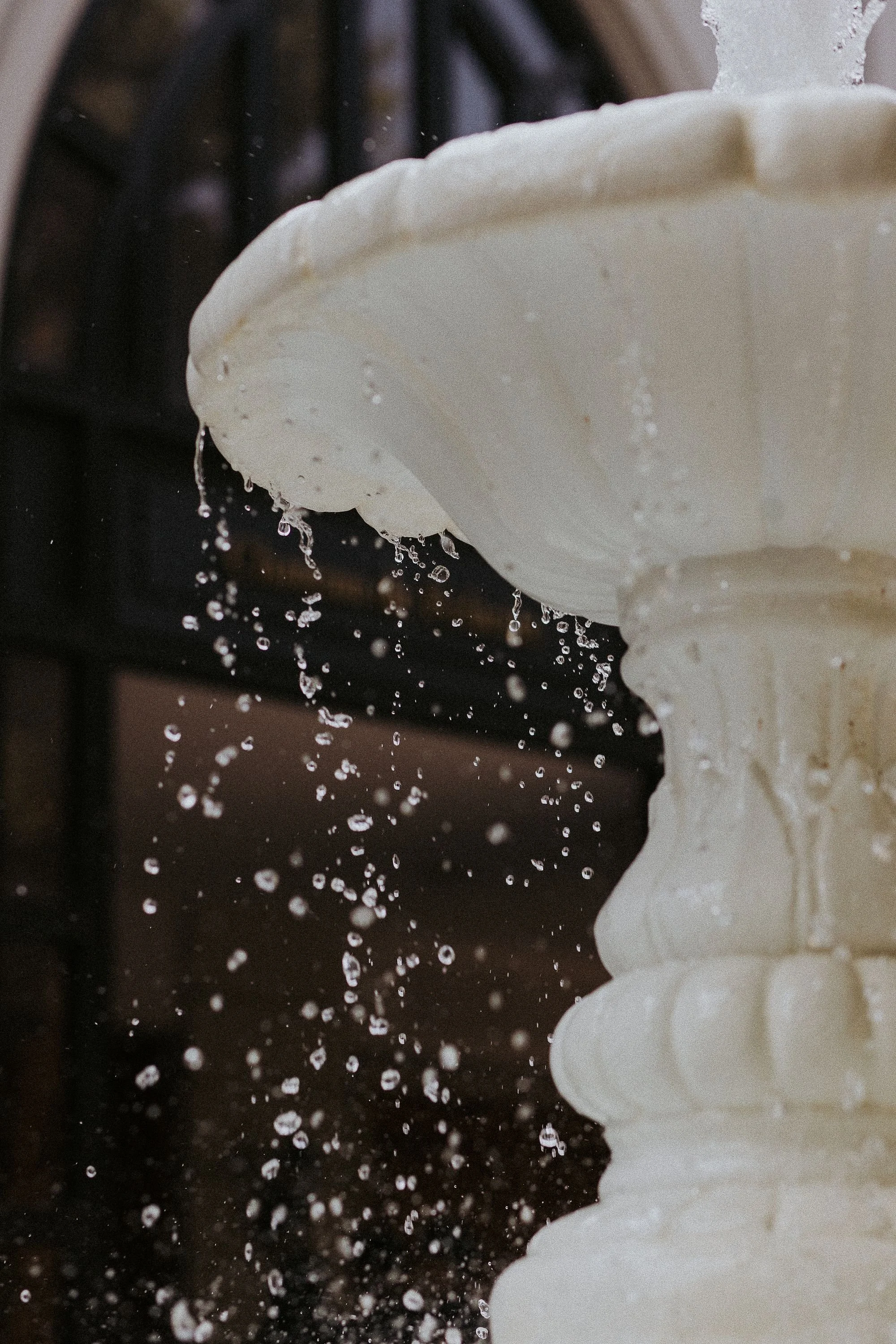 Close-up of a white cup with hot water pouring into it, with water splashing and droplets falling, with a dark background.