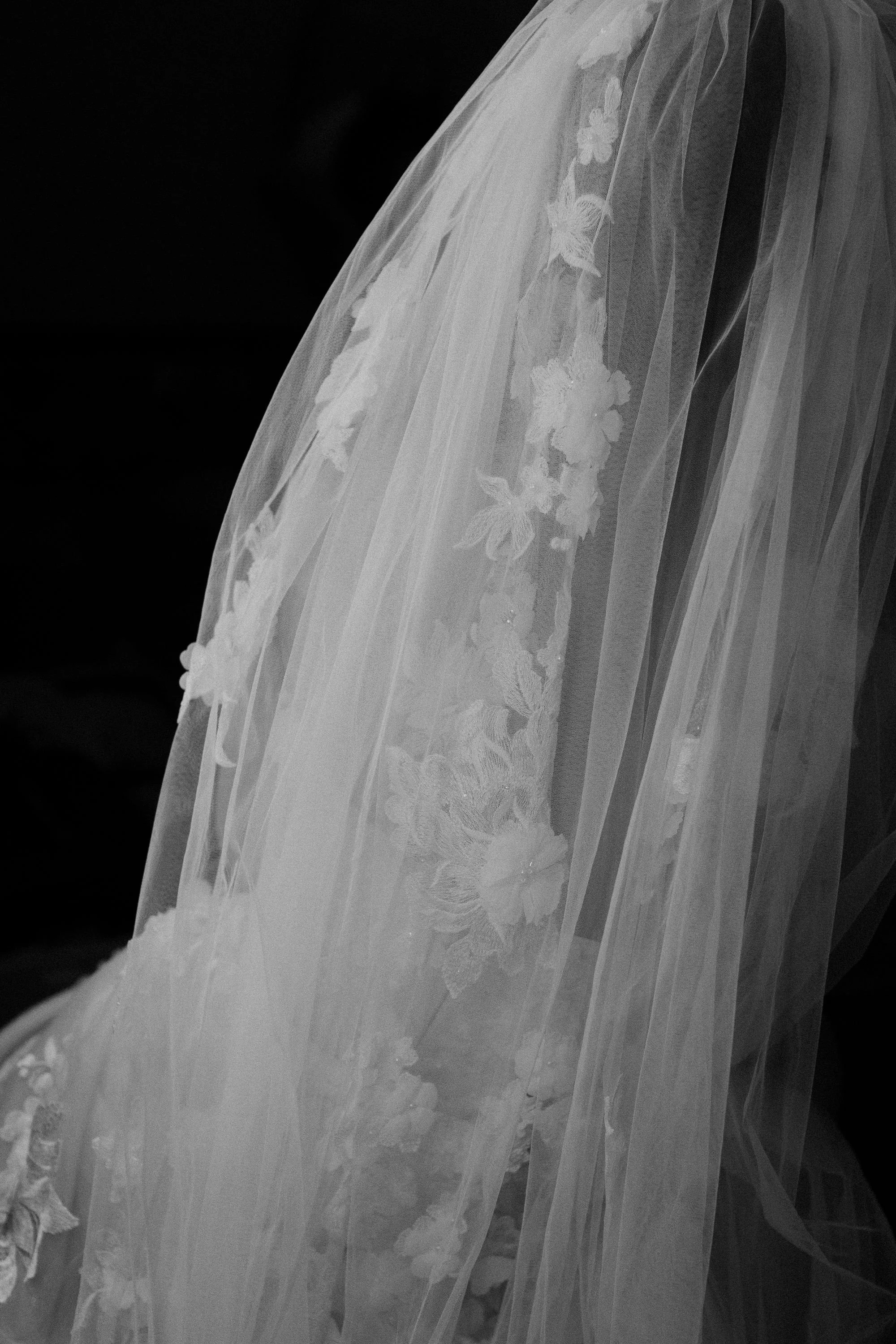 Close-up of a wedding dress with floral embroidery and lace details on sheer fabric, flowing down in soft layers.