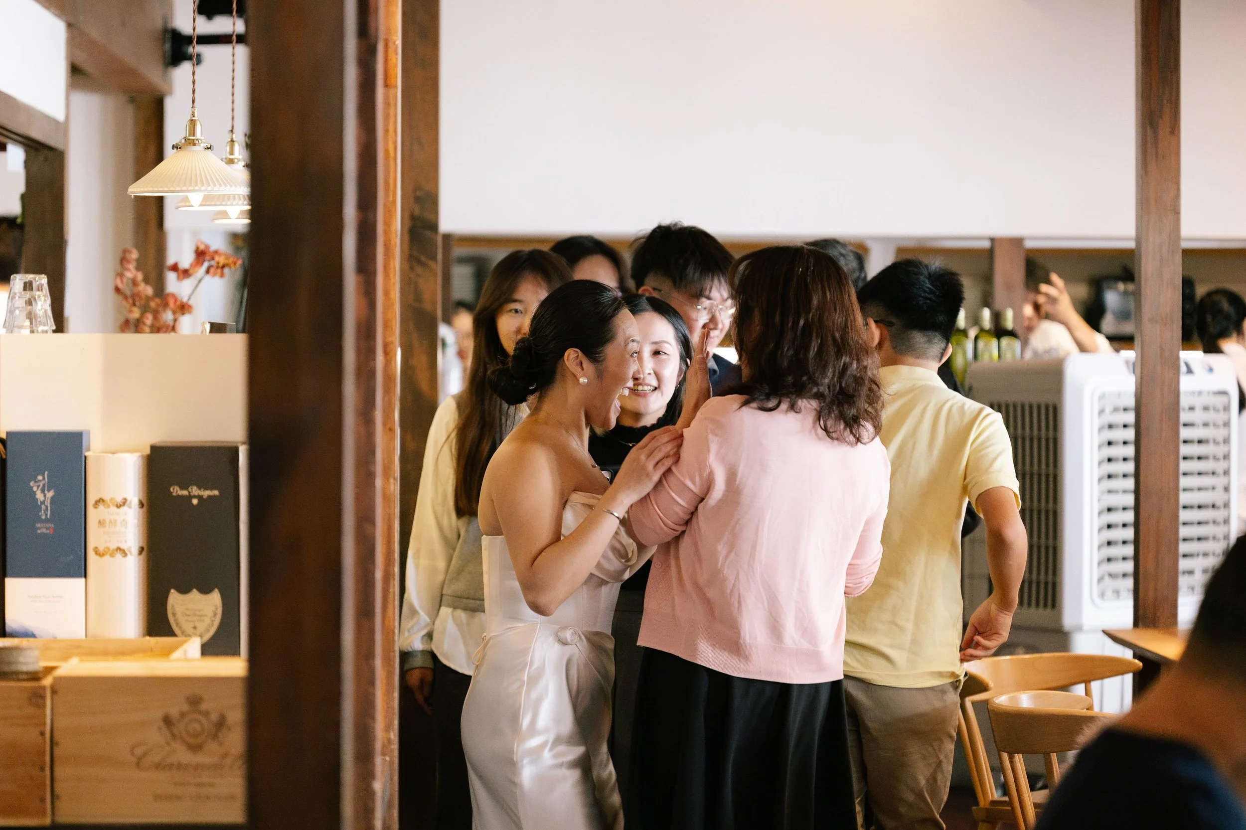 A group of people gathered together, smiling and engaging in conversation inside a warmly lit restaurant or cafe.