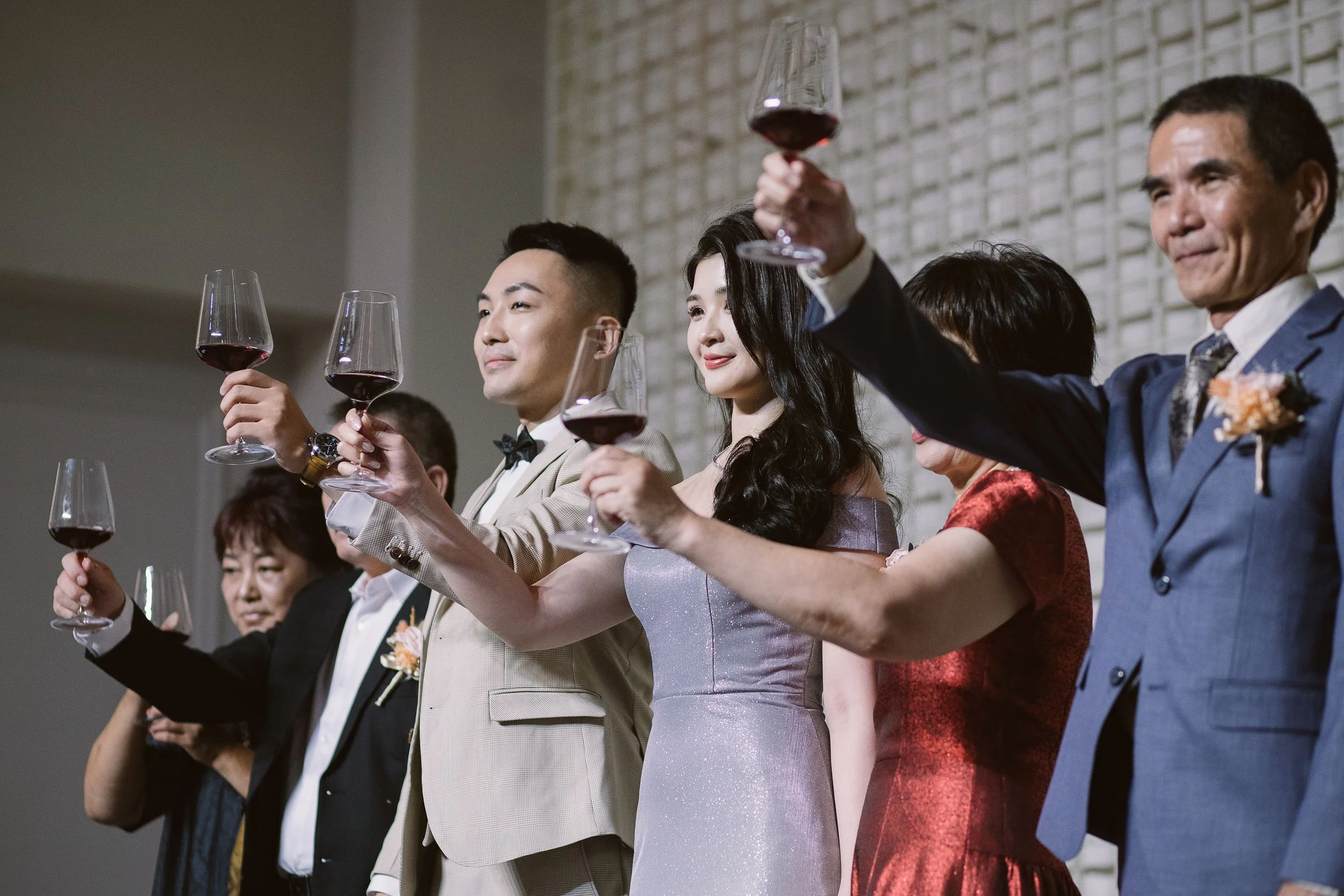 People in formal attire raising glasses of red wine in celebration at a banquet.