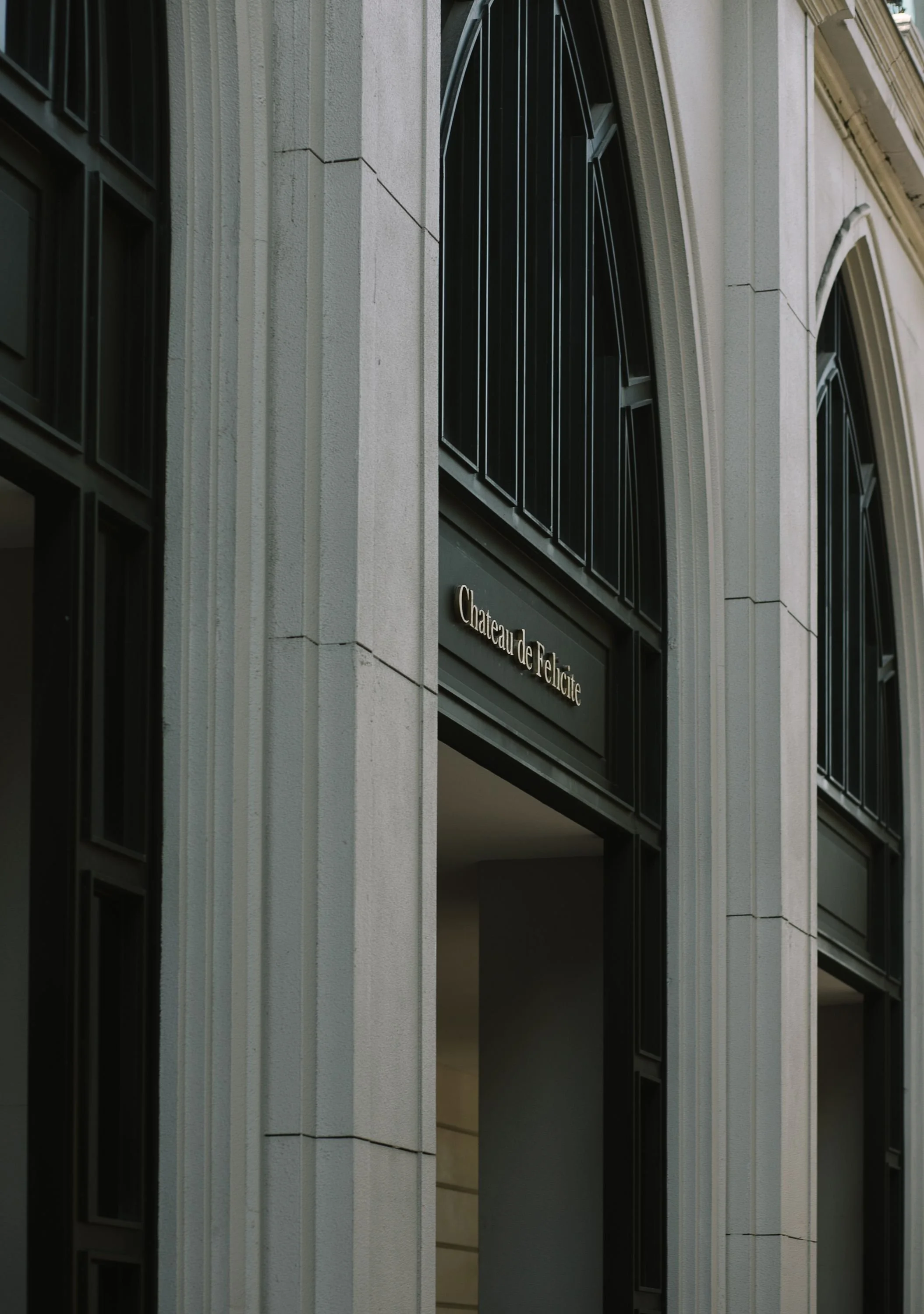 The image shows the exterior of a building with a sign that reads 'Chateau de Felicite'. The building has light-colored stone walls and large arched windows with black framework.