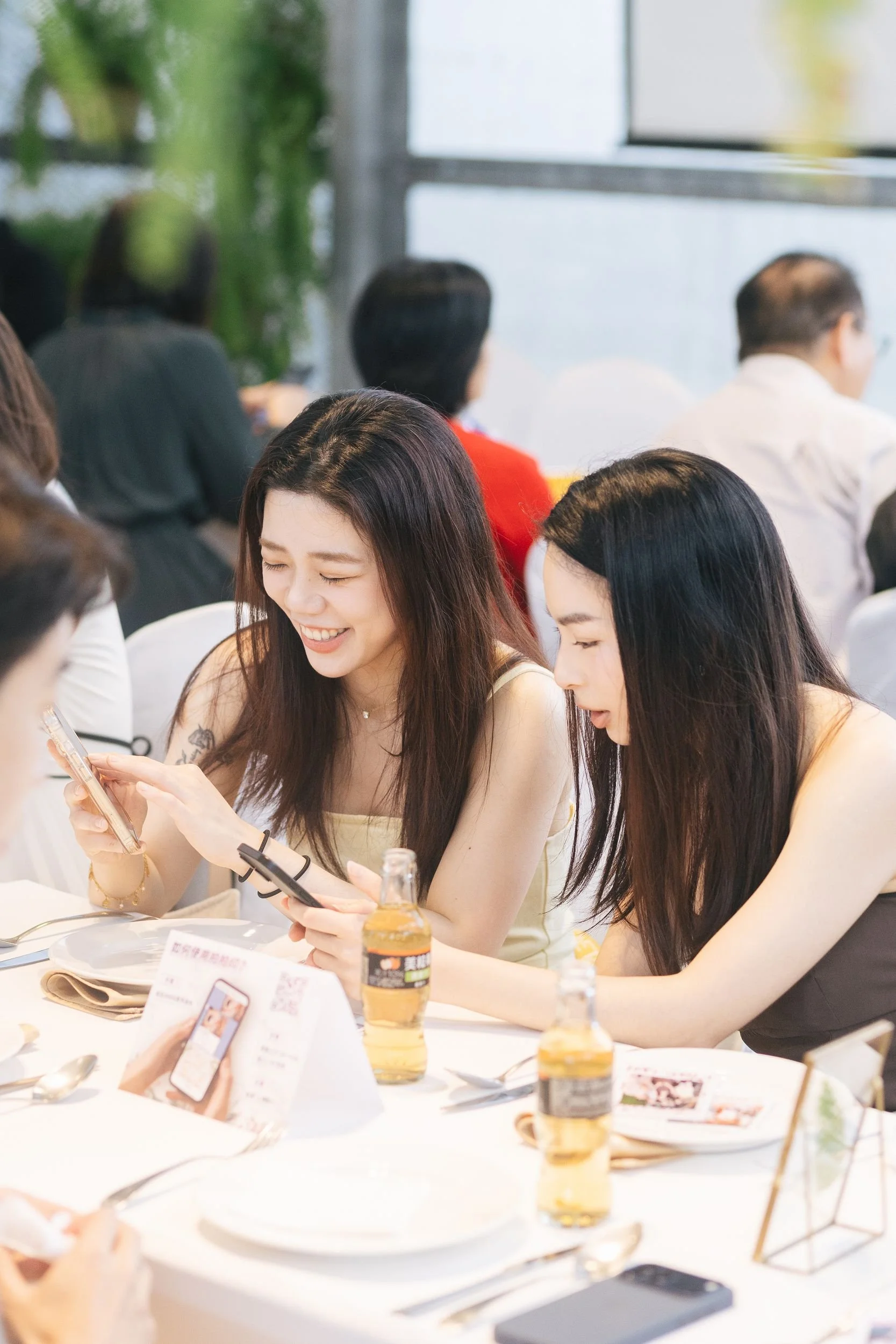 People sitting at a table in a bright room, some looking at their phones, with drinks and paper menus on the table.