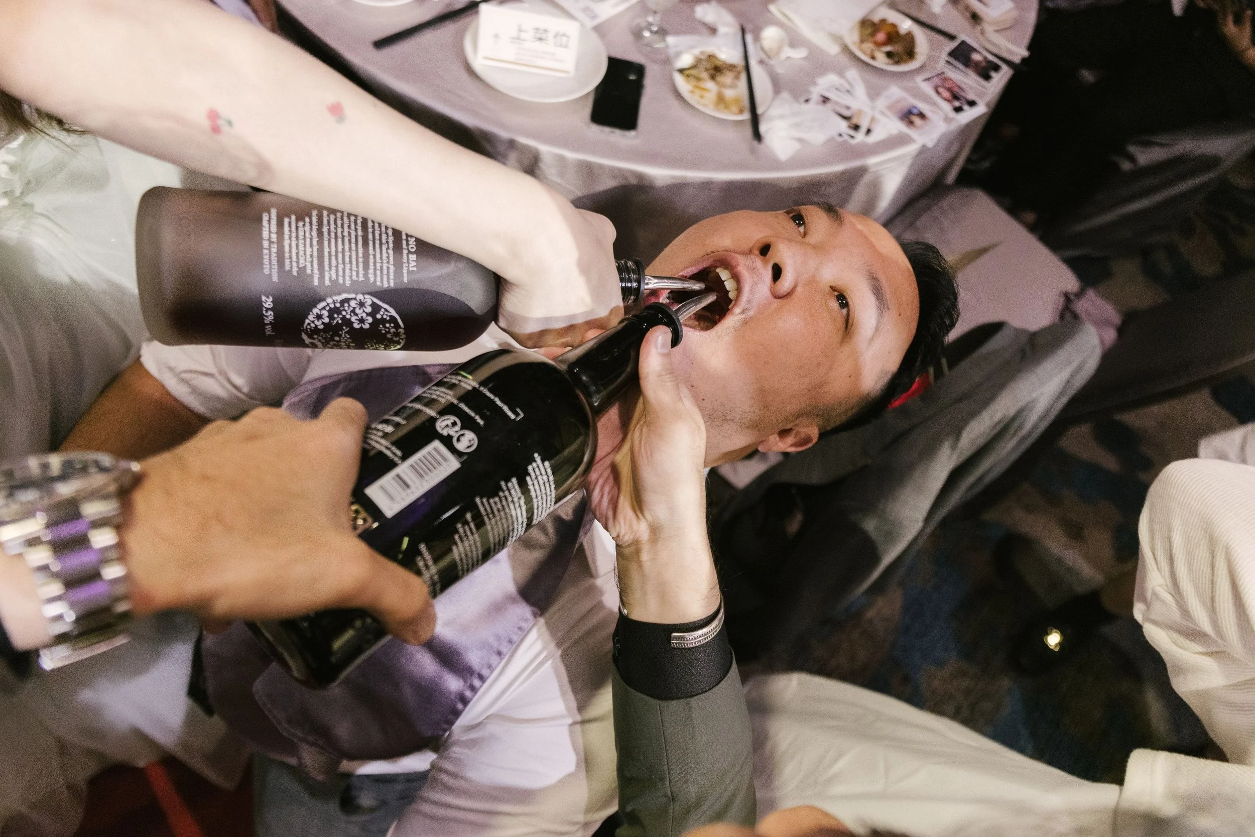 A man is receiving oral sushi-style food from a person wearing a white glove at a dining table.