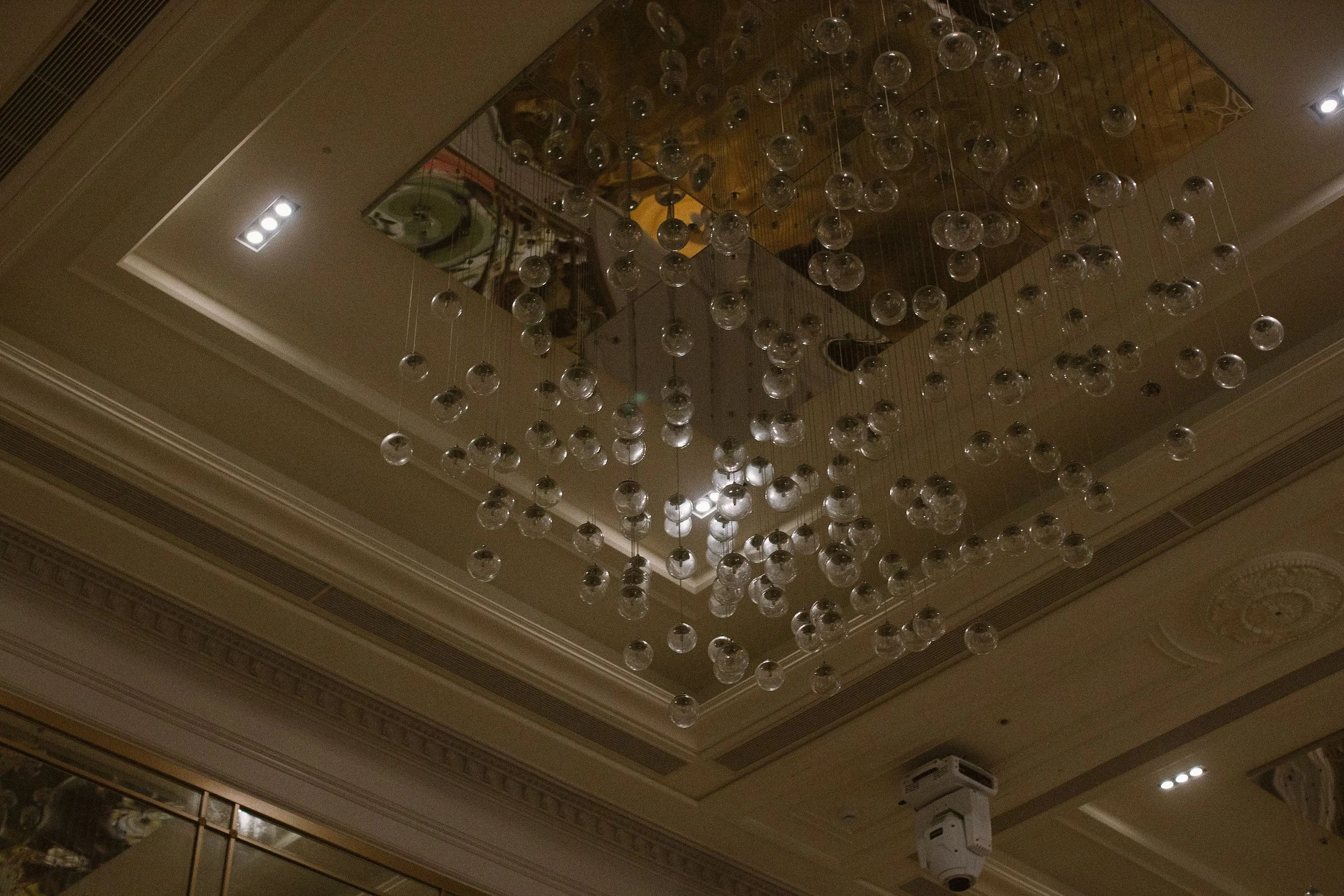 A chandelier made of numerous spherical glass bulbs hangs from a wooden ceiling in a decorated indoor space.