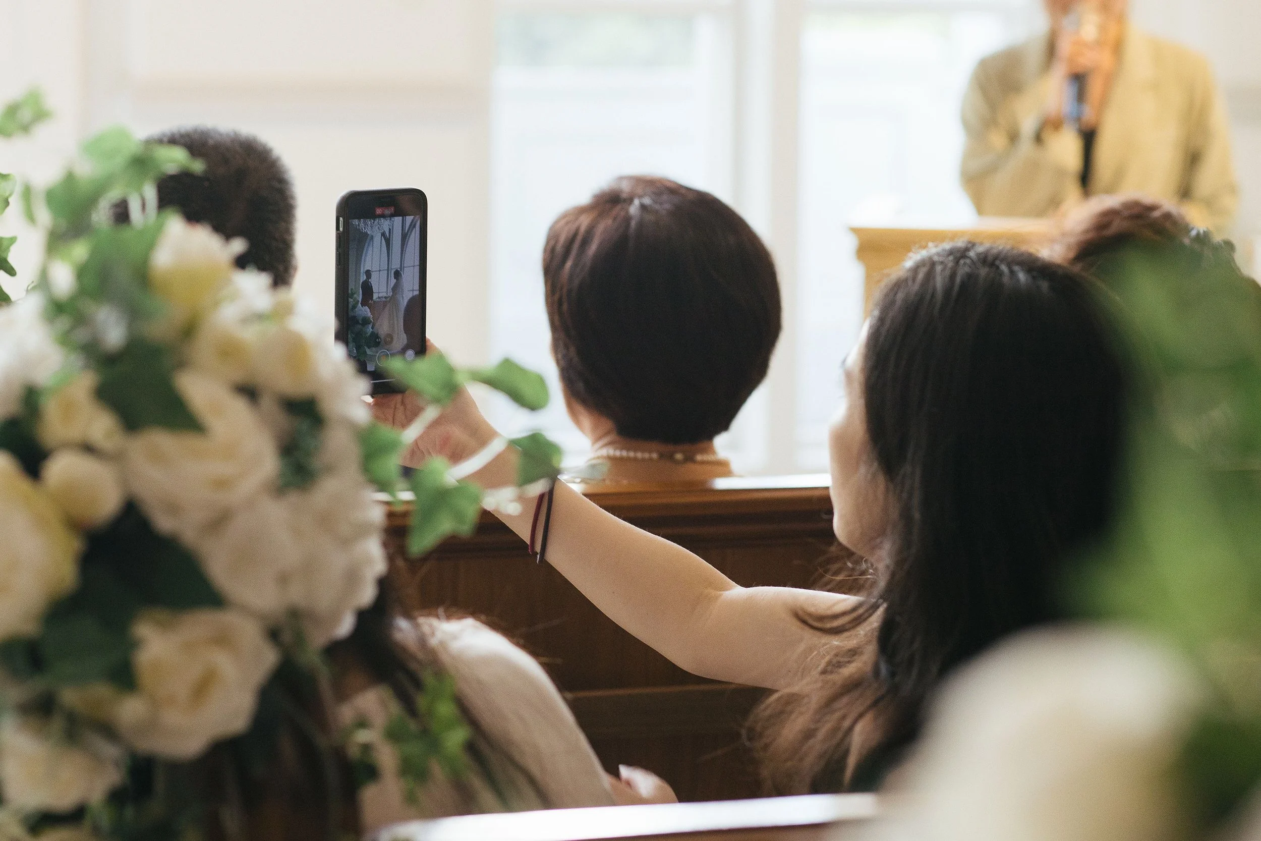 People at a wedding ceremony taking photos of the bride and groom, with floral decorations in the foreground.