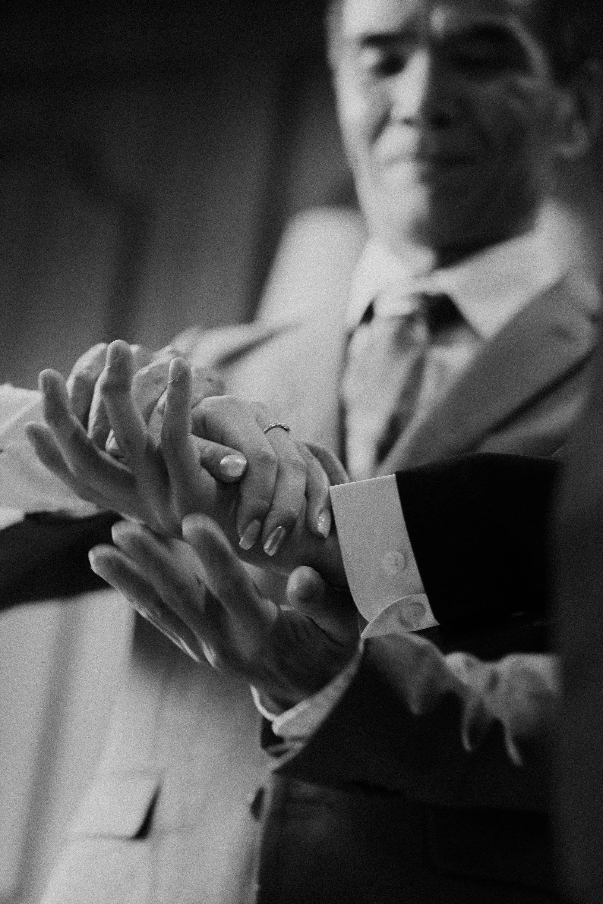 Close-up of a man in a suit adjusting his cuffs, with a blurred background.