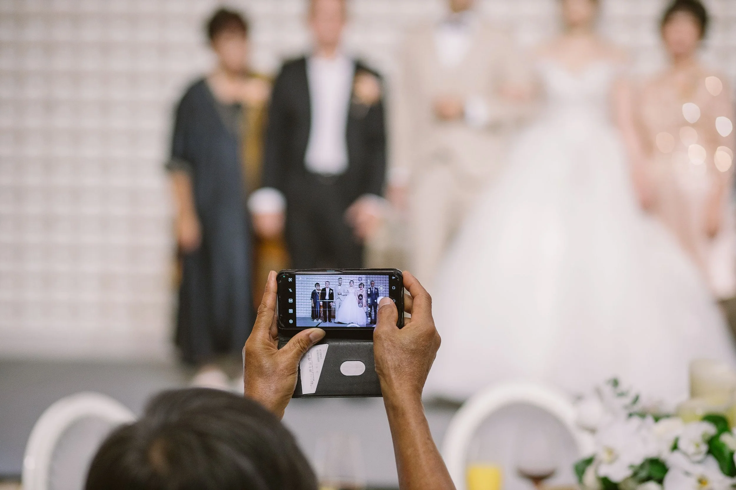 Person taking a photo of a wedding couple with a smartphone at a wedding reception.