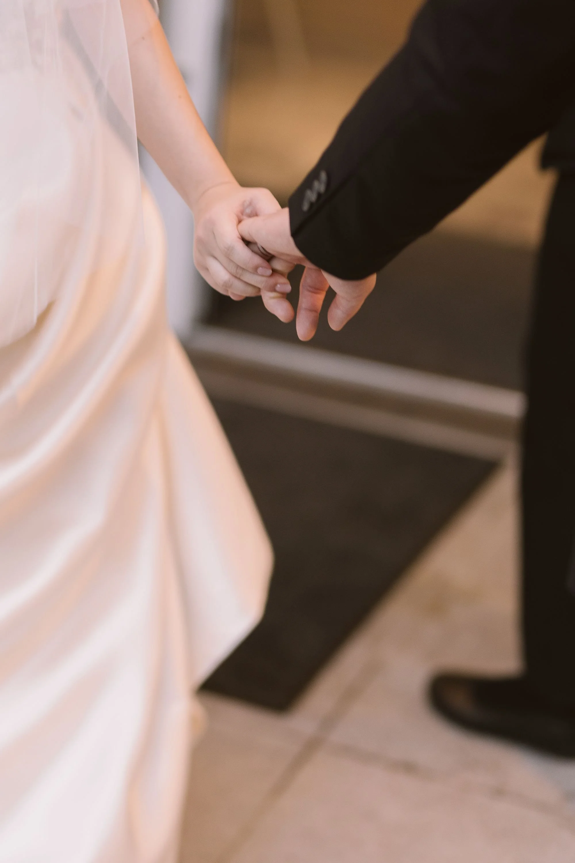 A couple holding hands, with one person in a light pastel dress and the other in a dark suit.