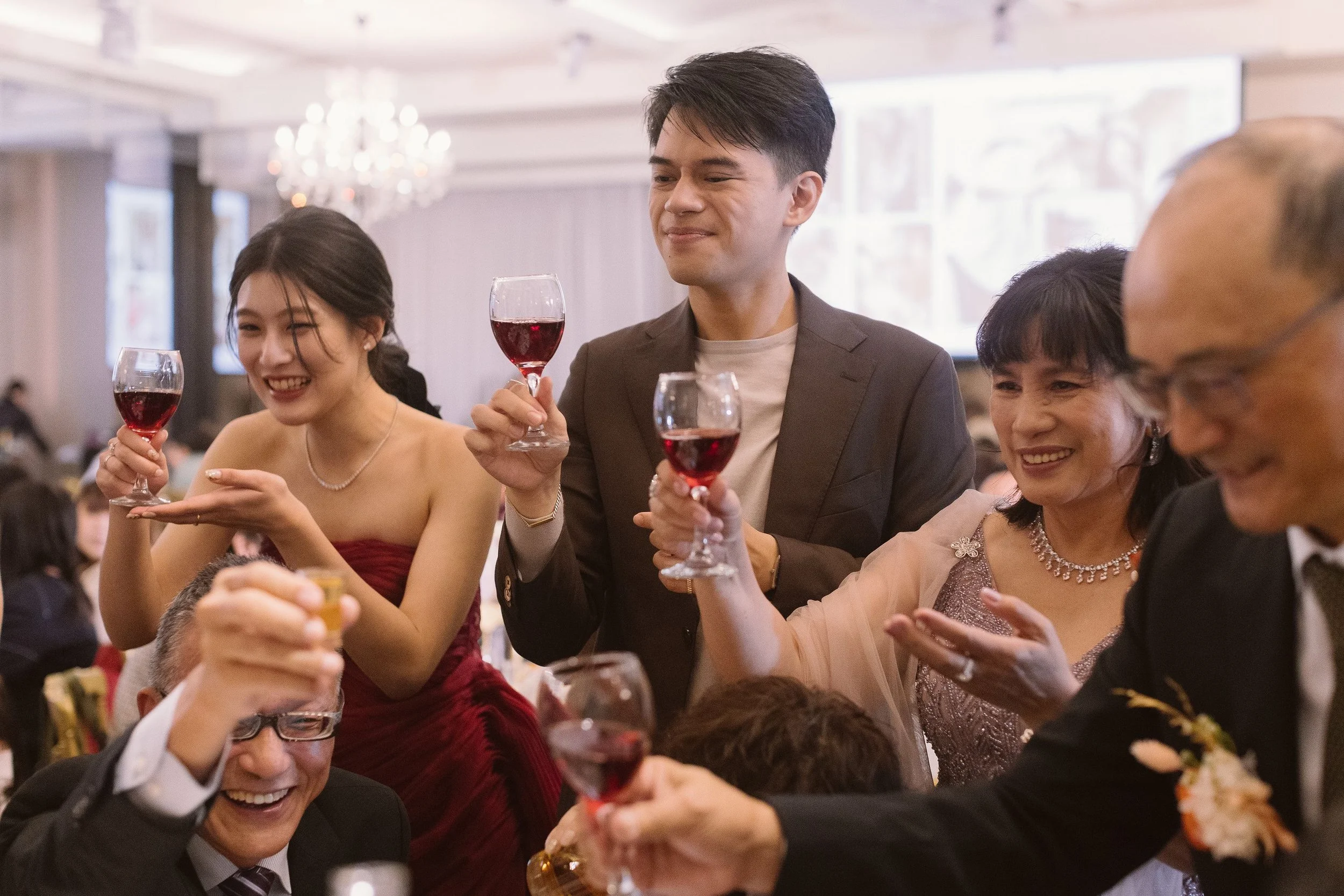 People at a celebration making a toast with glasses of red wine, smiling and enjoying the event in an elegant setting.