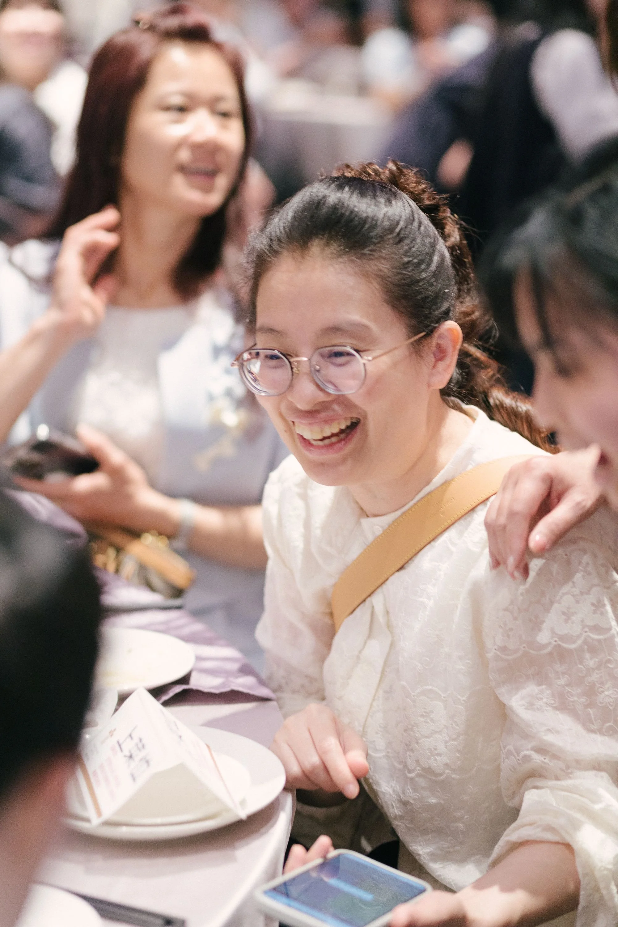 People smiling and interacting at a social gathering or event, with one woman holding a smartphone.