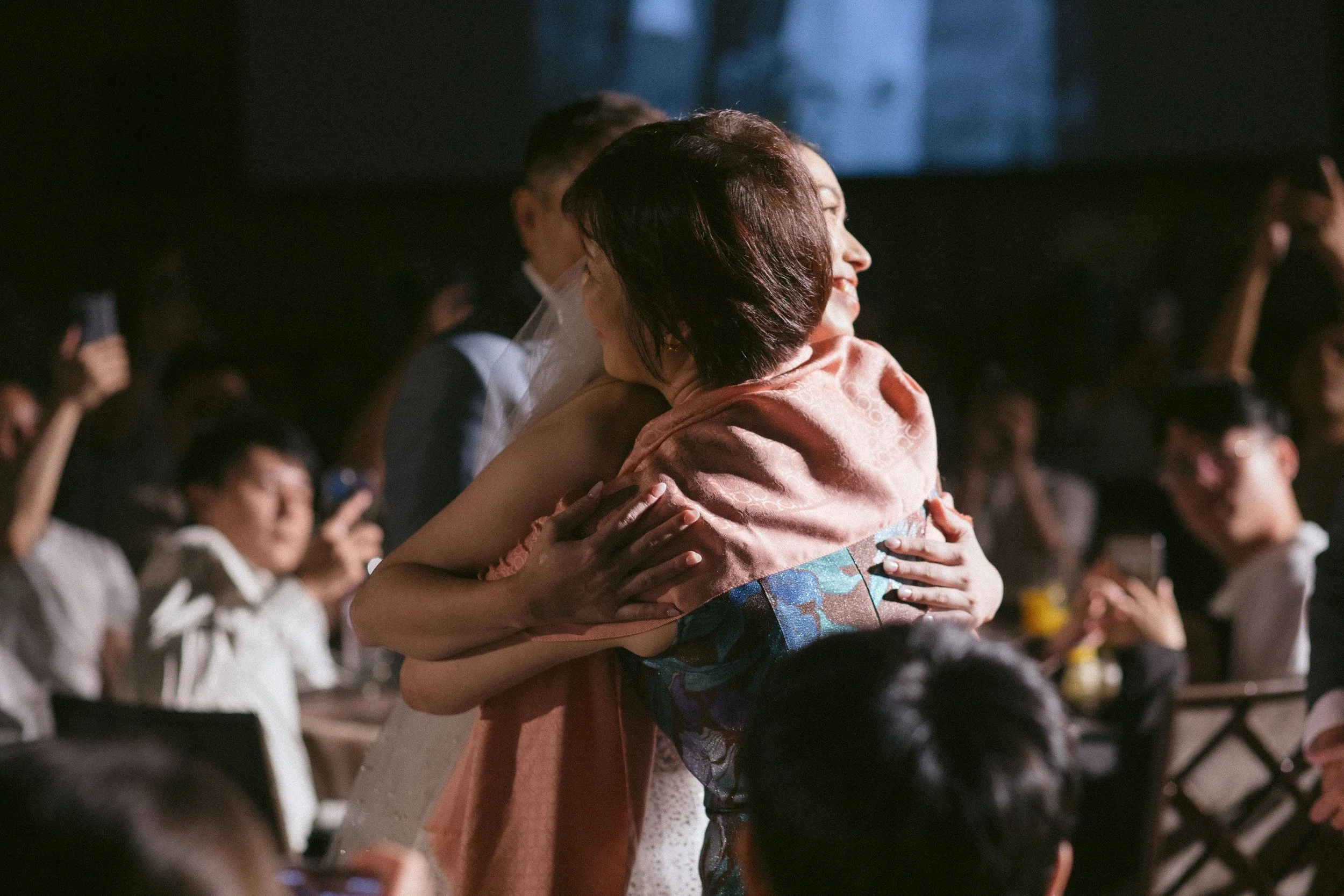 A woman in traditional Japanese kimono hugging someone in a crowded event or ceremony.