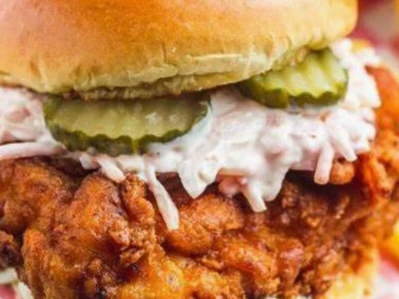 Close-up of a fried chicken sandwich with pickles, coleslaw, and a bun.