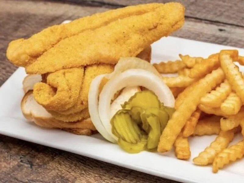 Fried fish fillet with French fries, sliced onions, and pickles on a white plate