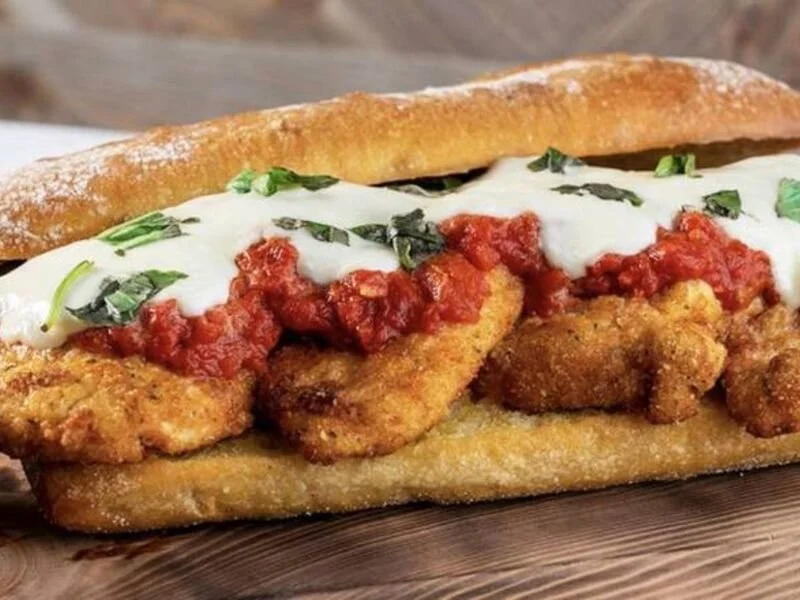 Fried chicken sandwich with tomato sauce, sour cream, and chopped herbs on a toasted bun.