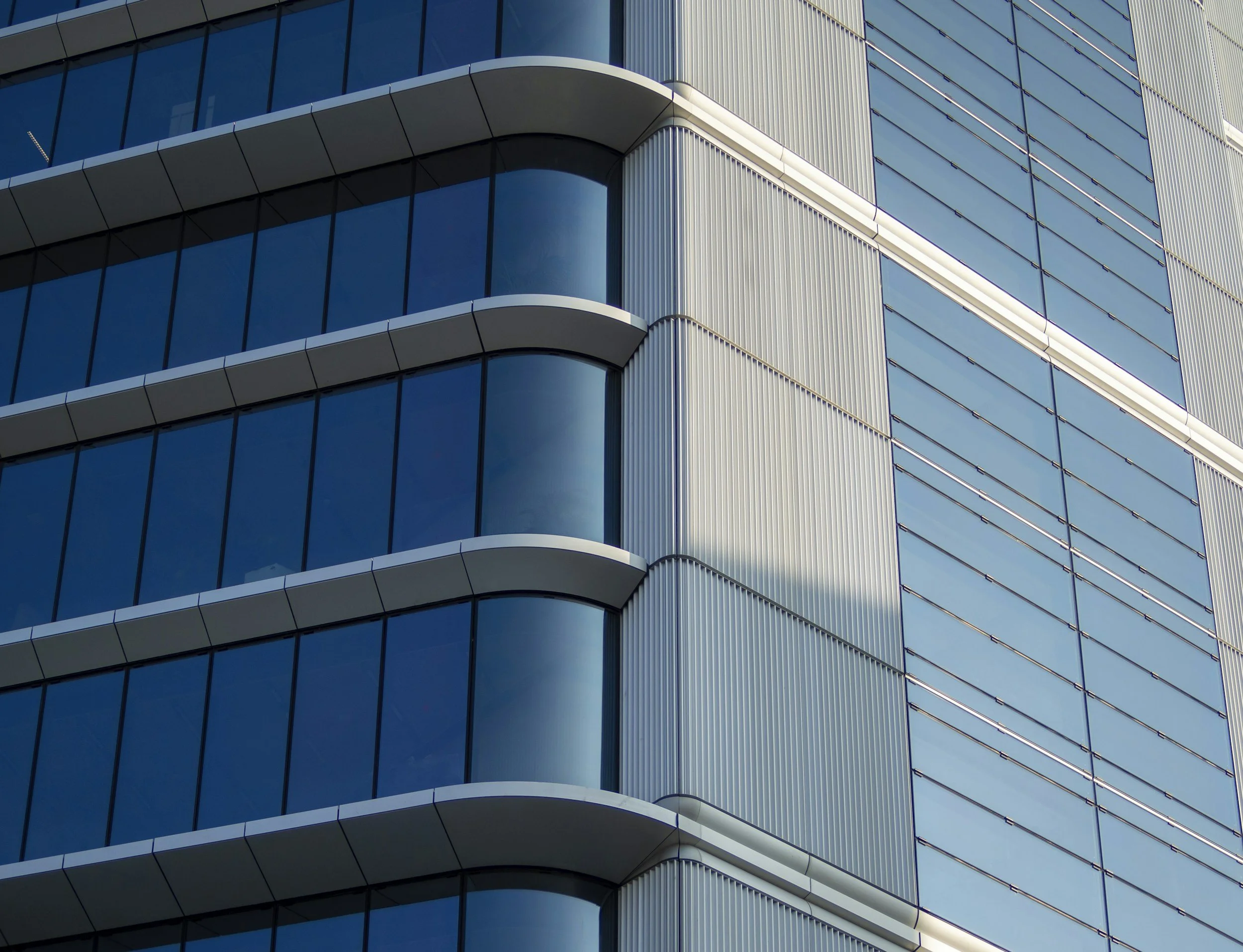 Close-up of a modern building's exterior with blue glass windows, white horizontal and vertical structural elements, and rounded balconies.