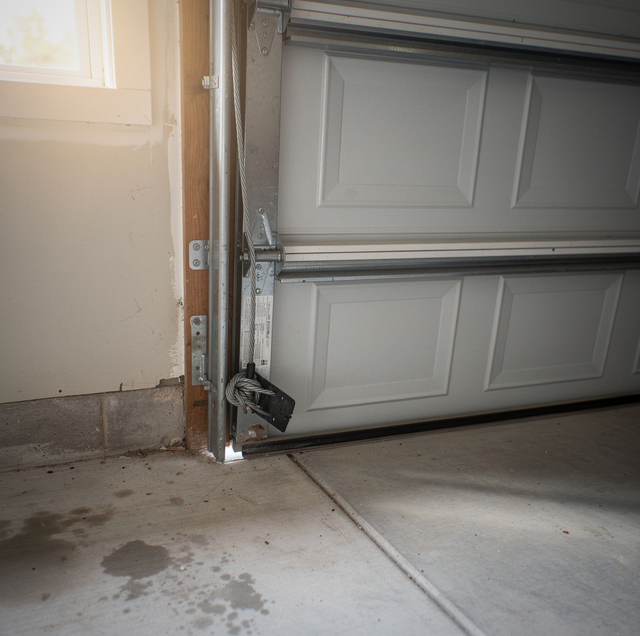 A white garage door with metal frame partially open next to a wooden door frame on a concrete floor.