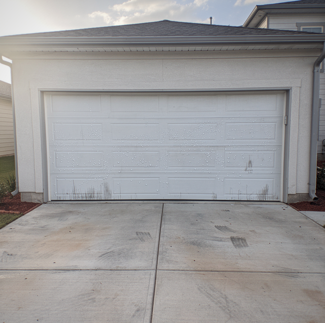 A white garage door on a white house with a concrete driveway in front.