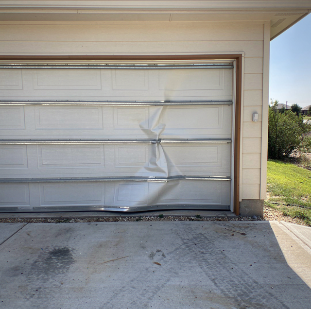 White garage door with metal tracks on concrete driveway with lawn and trees visible beyond.
