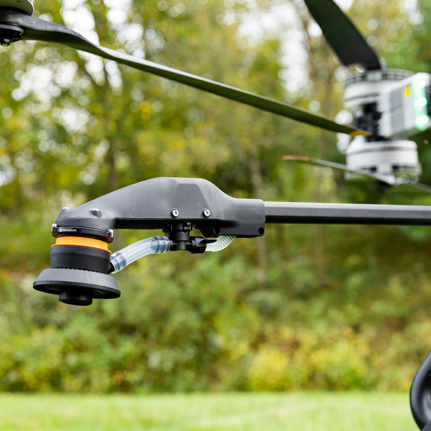 Close-up of a drone's camera and gimbal system with a blurred outdoor background of trees and greenery.