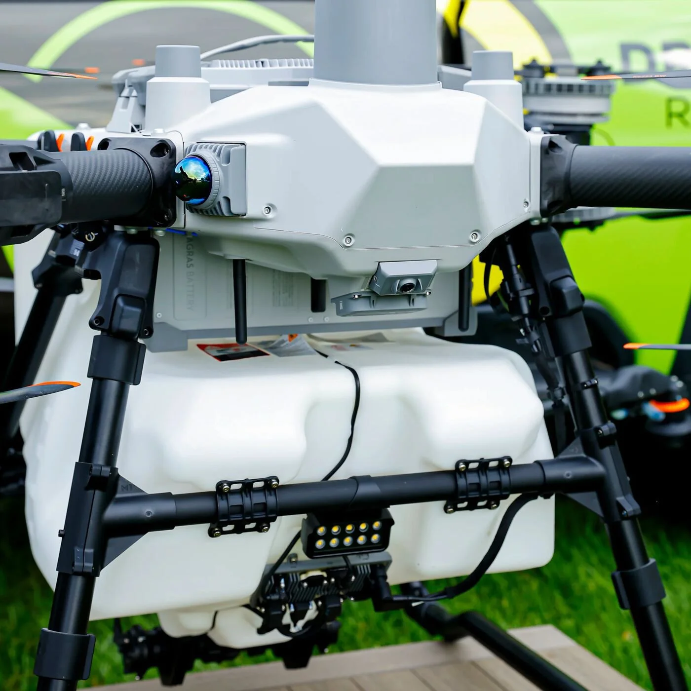 Close-up of a drone with a white body, black propellers, and various sensors and cameras mounted on it, outdoors on grass.