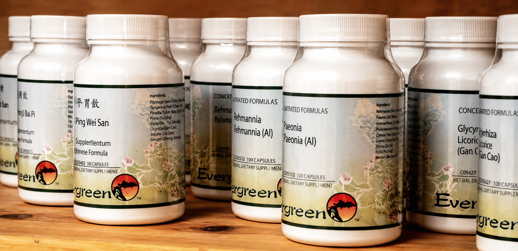 Several bottles of Chinese herbal medicine dietary supplements labeled with ingredients and brand name, lined up on a wooden surface.