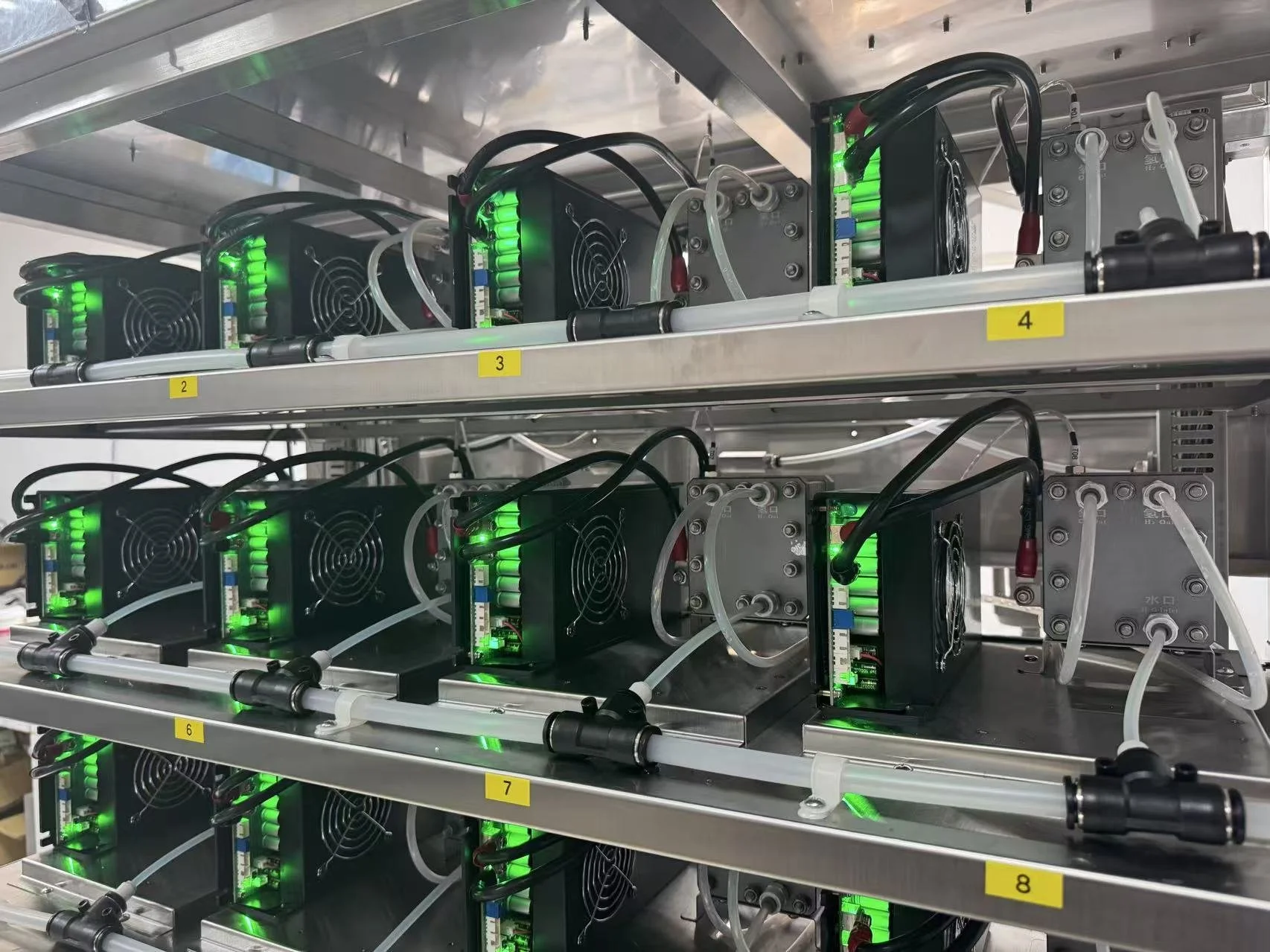 Multiple cryptocurrency mining rigs with power supplies and cooling fans, arranged on metal shelves labeled with yellow tags numbered 2 to 8, with green indicator lights on the mining devices.