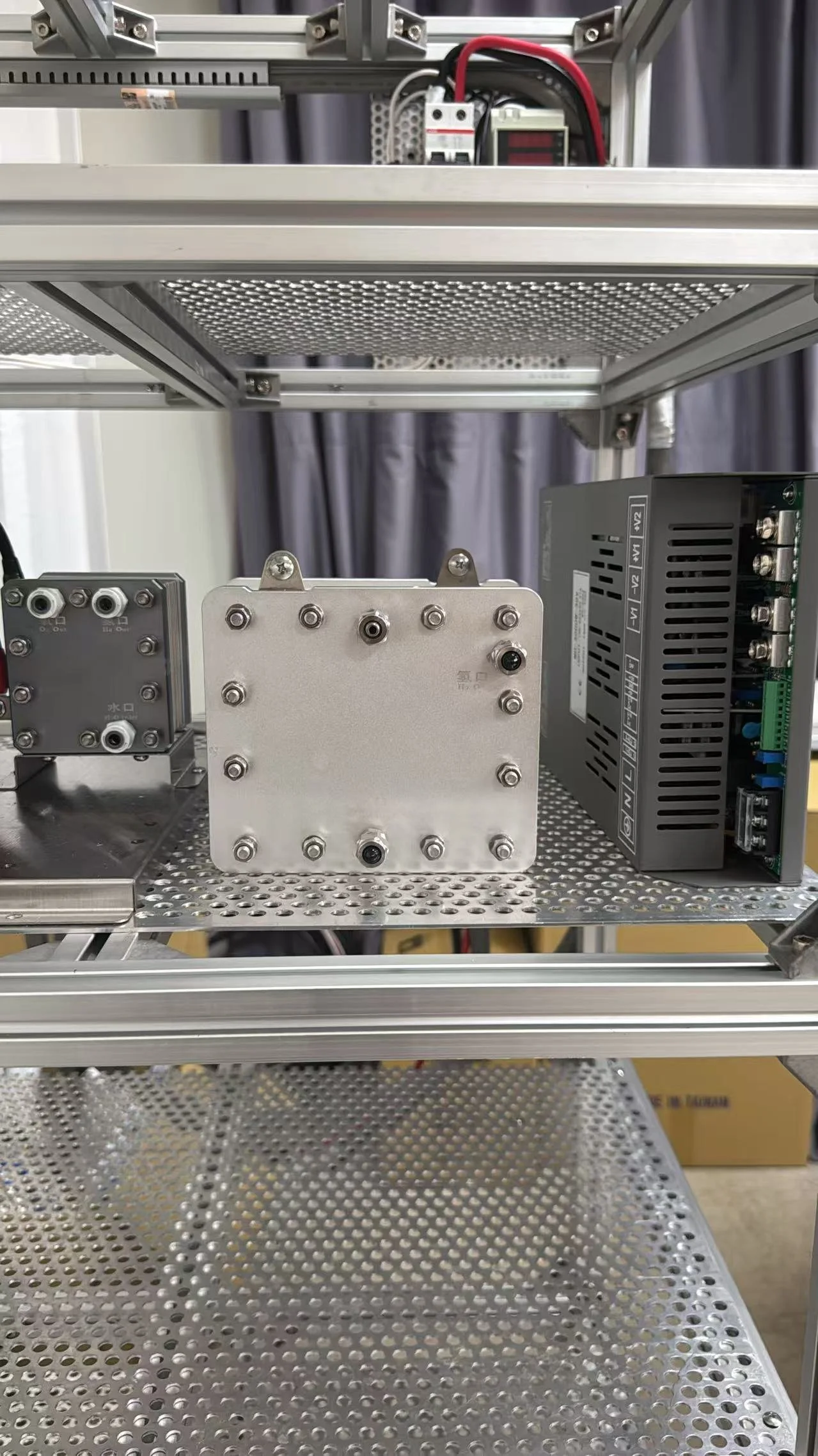 Metal electronics enclosure with circuit boards, power supplies, and wiring mounted on a perforated metal rack in a laboratory or industrial setting.