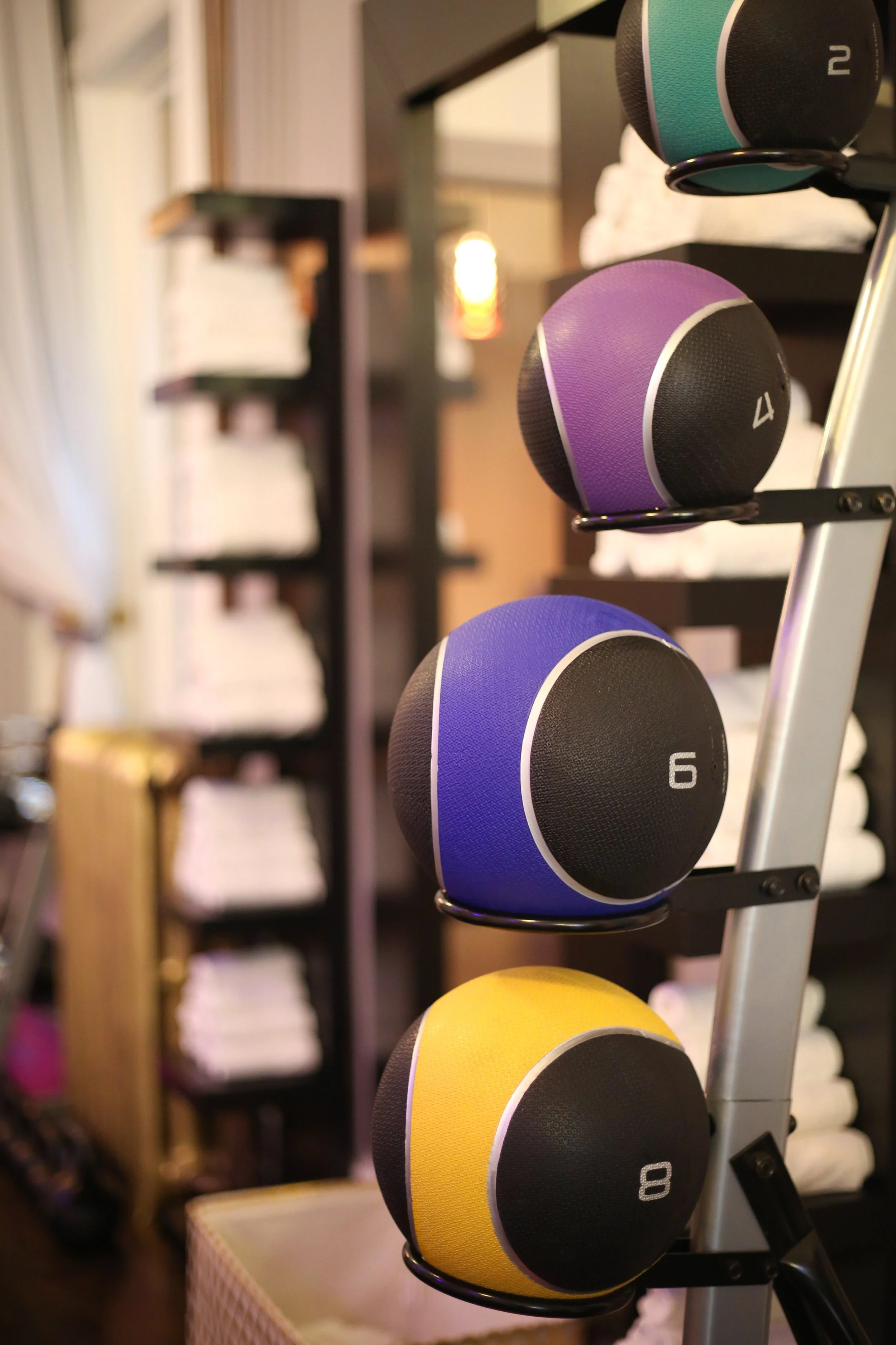 Colorful medicine balls numbered 2, 4, 6, 8, and 10 placed on a metal rack in a gym or fitness studio.