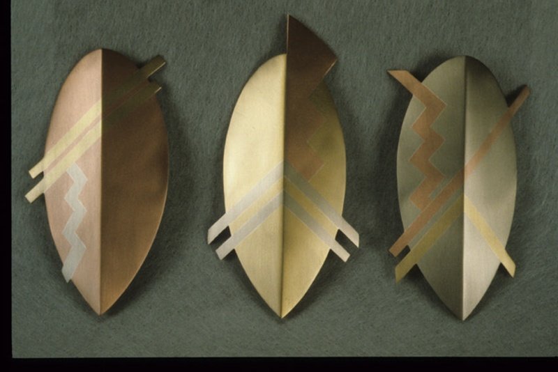 Three metallic wall sculptures with abstract designs mounted on a green wall.
