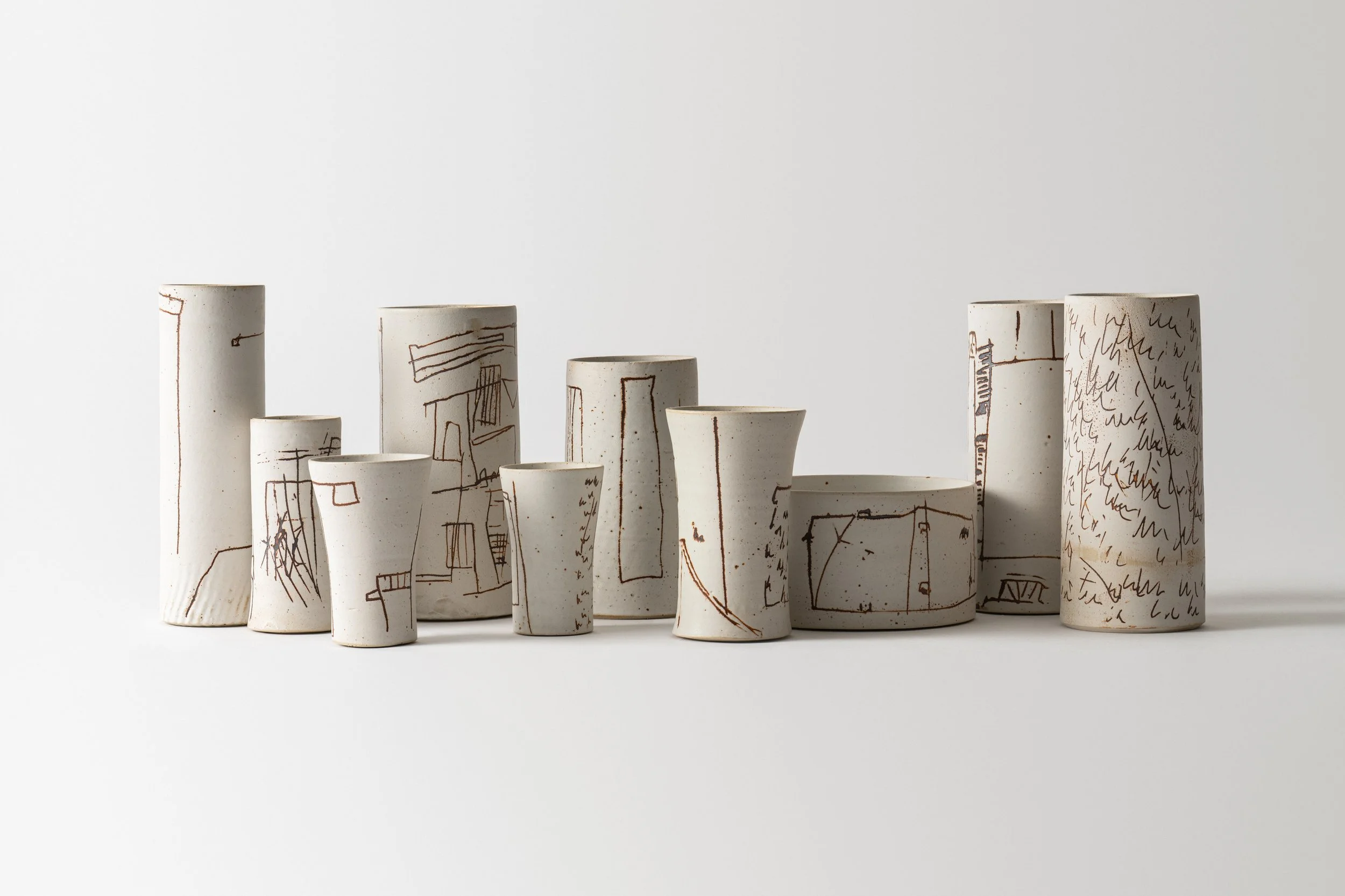 A collection of ceramic vases with abstract line drawings and scribbles on a white background.