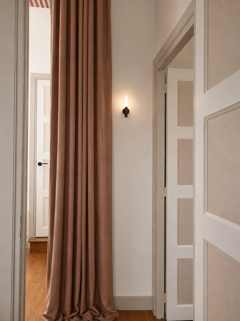 Palier de l'espace horizon. Un mur blanc avec une porte à droite, un rideau beige ou rose clair et un luminaire mural allumé.