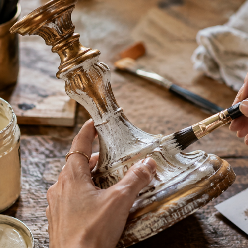 Une personne peint un ancien chandelier en bois avec de la peinture blanche lors d'un brunch atelier Maison Tourterelle