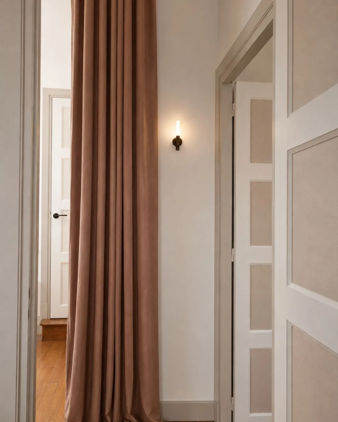 Vue intérieure du palier au 1er étage l'Horizon avec une porte blanche, un mur avec une applique murale moderne et un rideau en velours rose saumon.