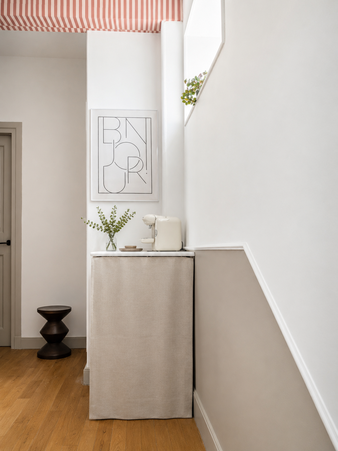 Coin café à l'étage de l'Horizon avec un meuble recouvert de tissu beige, une machine à café blanche, un vase avec des feuilles vertes, et une œuvre d'art graphique noire et blanche sur le mur.
