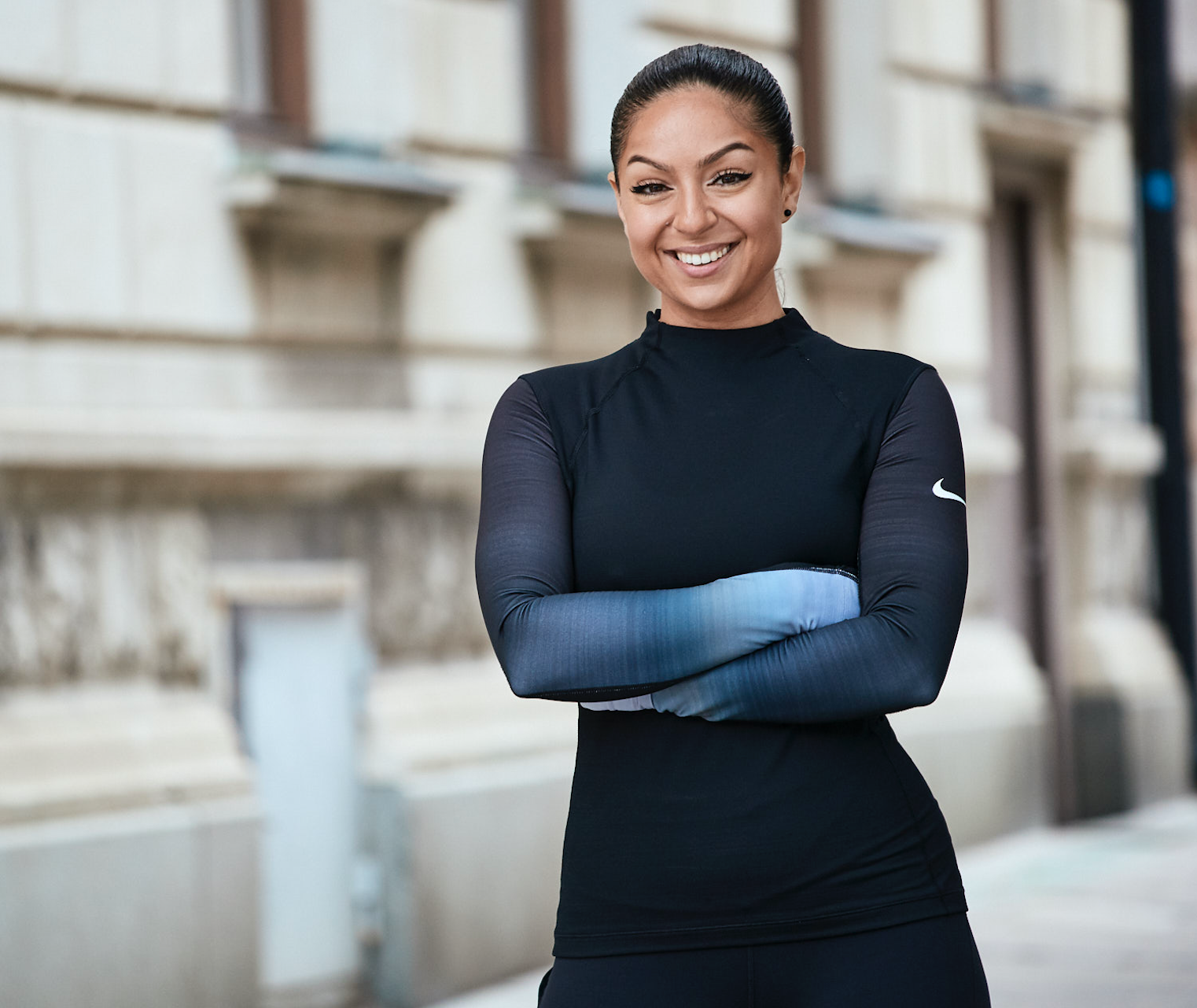 A smiling woman in athletic wear standing outdoors with her arms crossed.
