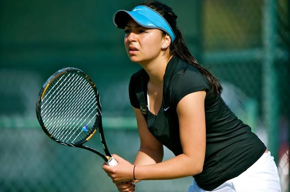 Tennis player wearing a blue visor and black shirt, holding a tennis racket, on a tennis court during a match.