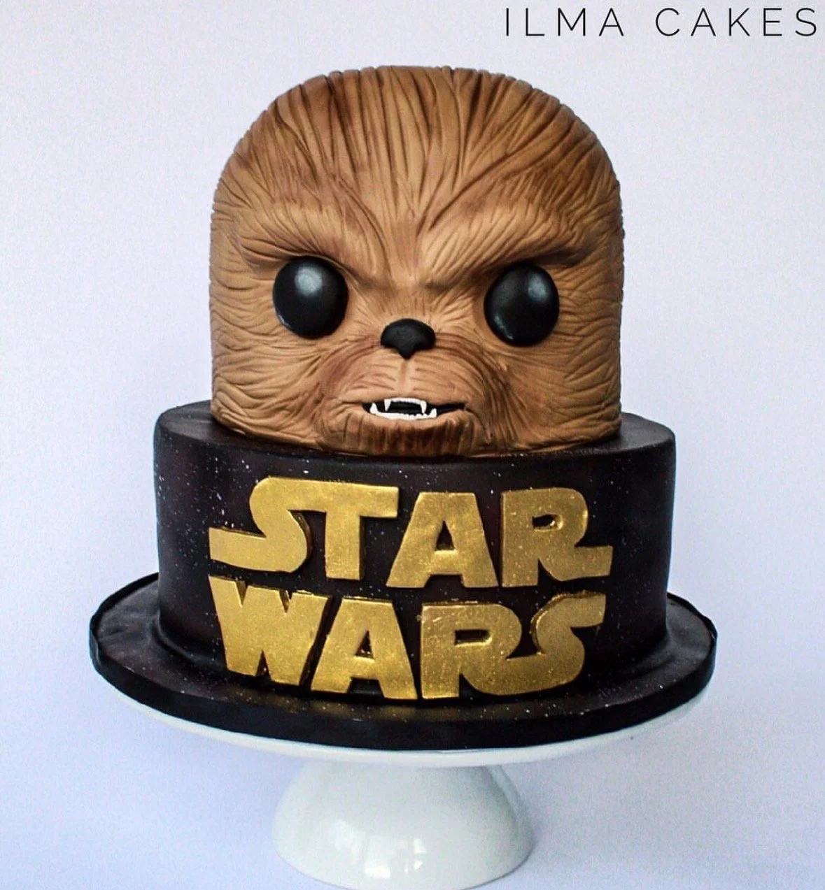 a movie franchise themed cake with a Chewwy figure on top and gold lettering on a black base