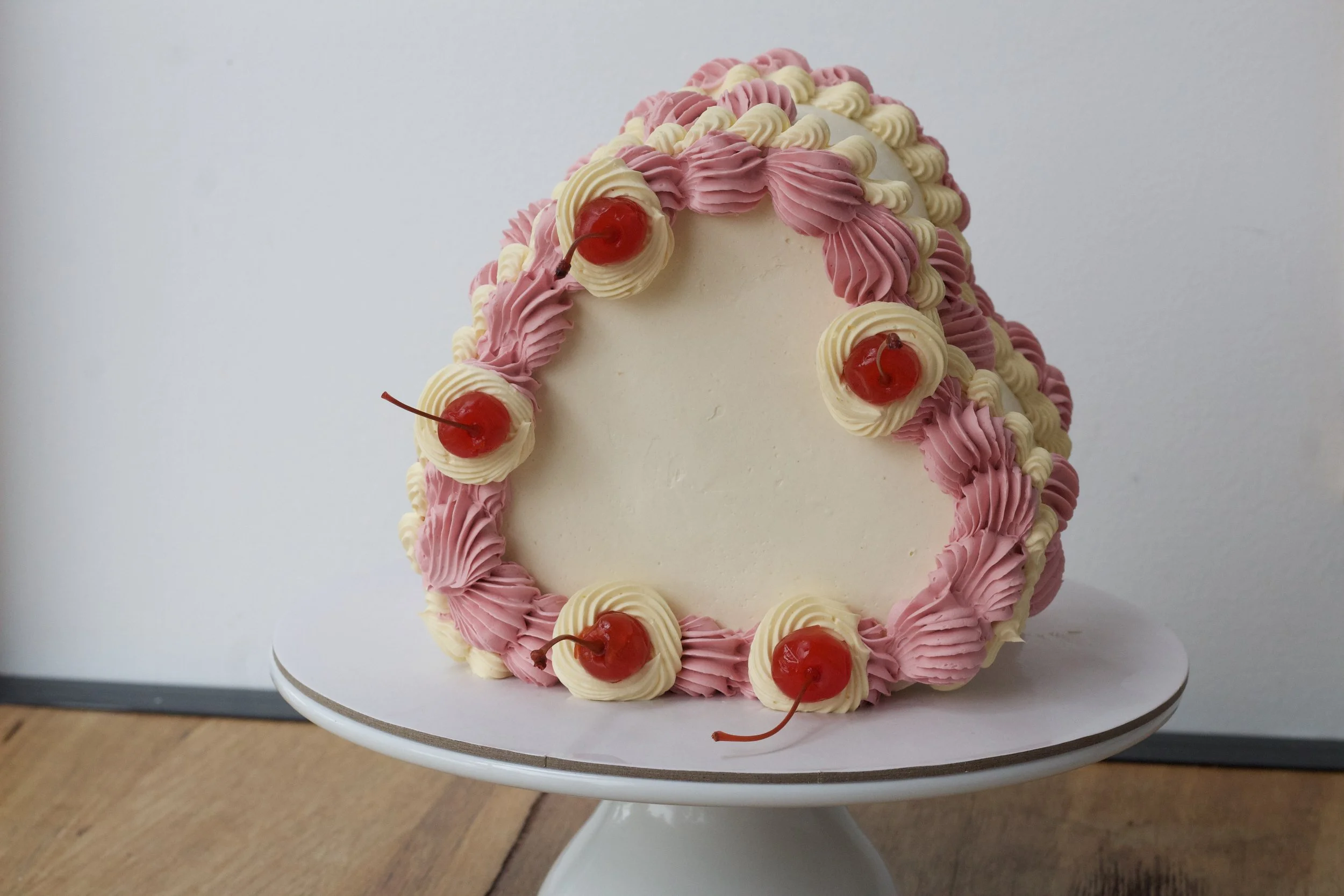 A white frosted cake decorated with pink and white piped swirls and topped with maraschino cherries.