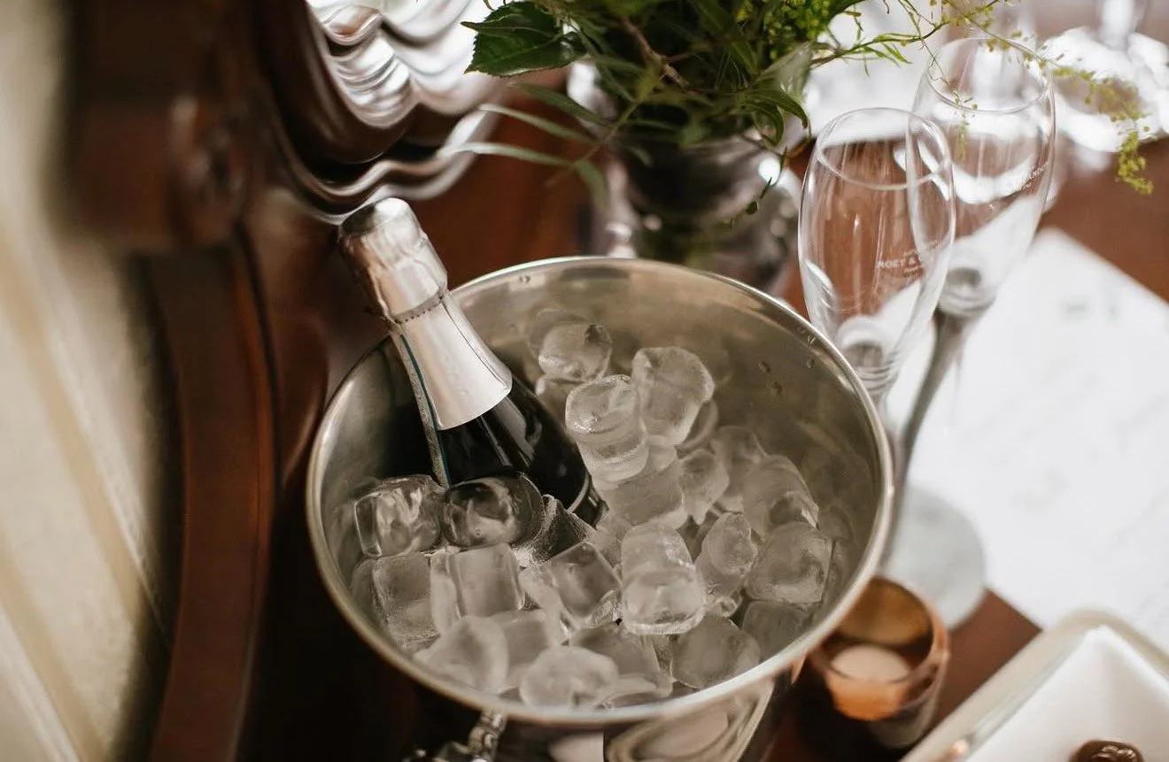A bottle of champagne chilling in an ice bucket surrounded by glasses and decorative items on a wooden table.
