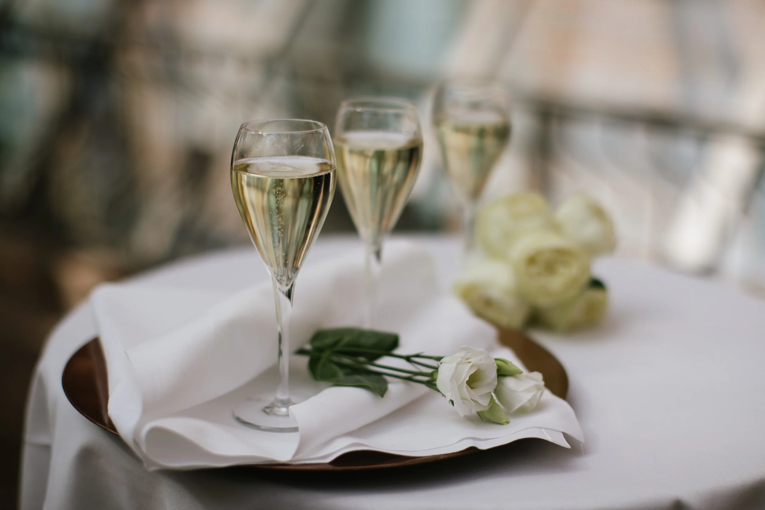 Two champagne glasses filled with sparkling wine on a white tablecloth, with white flowers and greenery nearby, suggesting a celebration or special event.