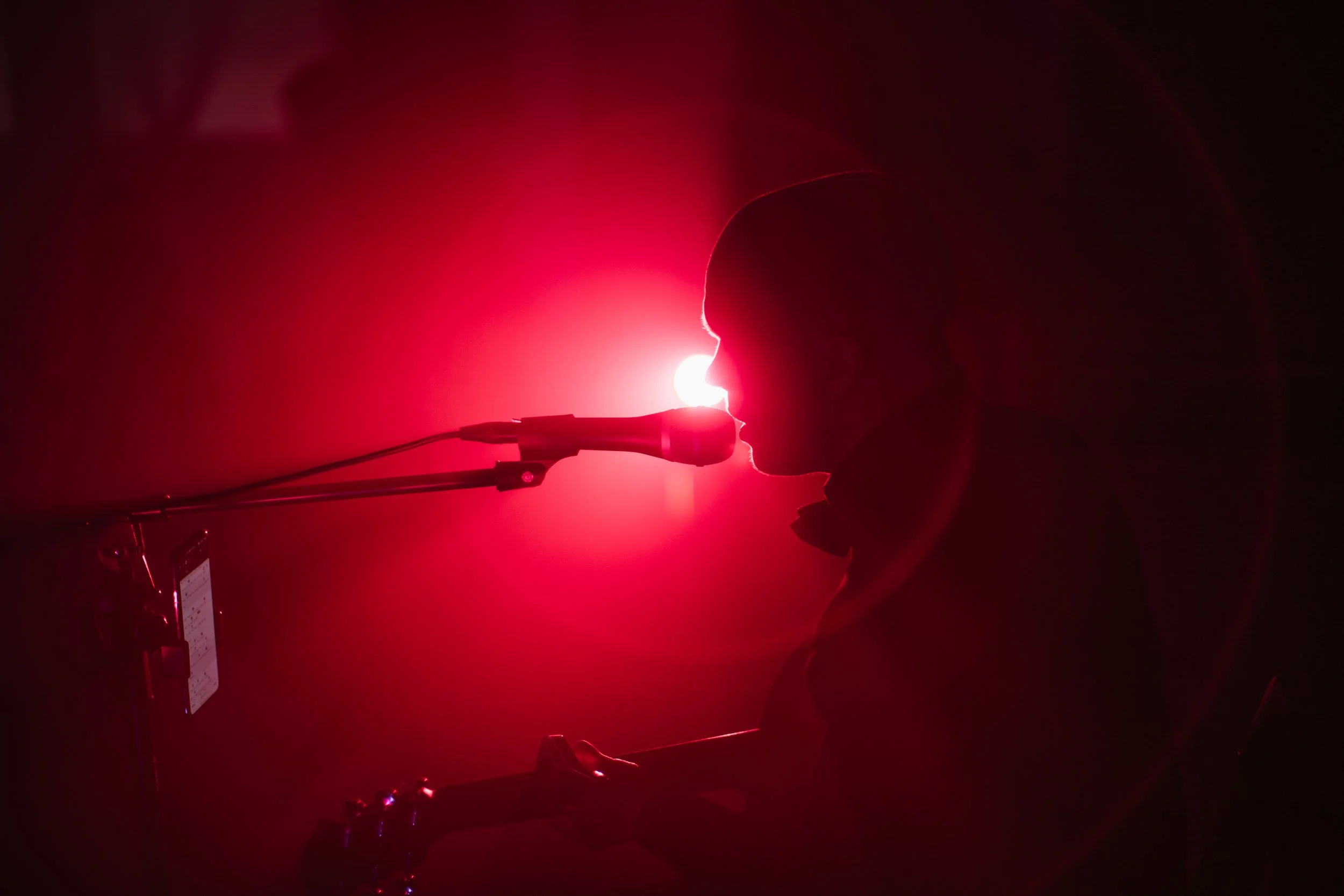 A person silhouette speaking into a microphone with a bright red light shining through their face, creating a dramatic shadow effect.