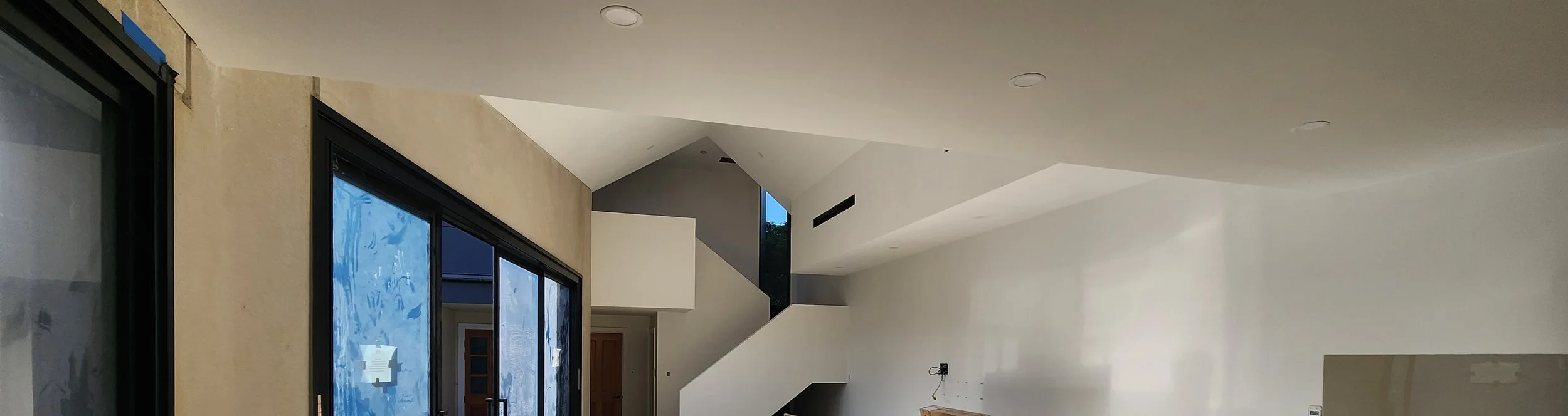 Empty modern living room with large sliding glass doors, staircase, and white walls.