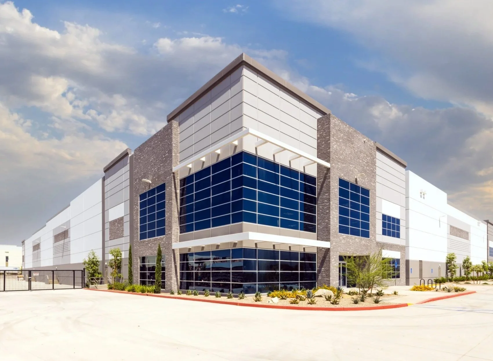 Modern commercial building with glass windows and brick accents, clear sky with some clouds, and landscaped surroundings.