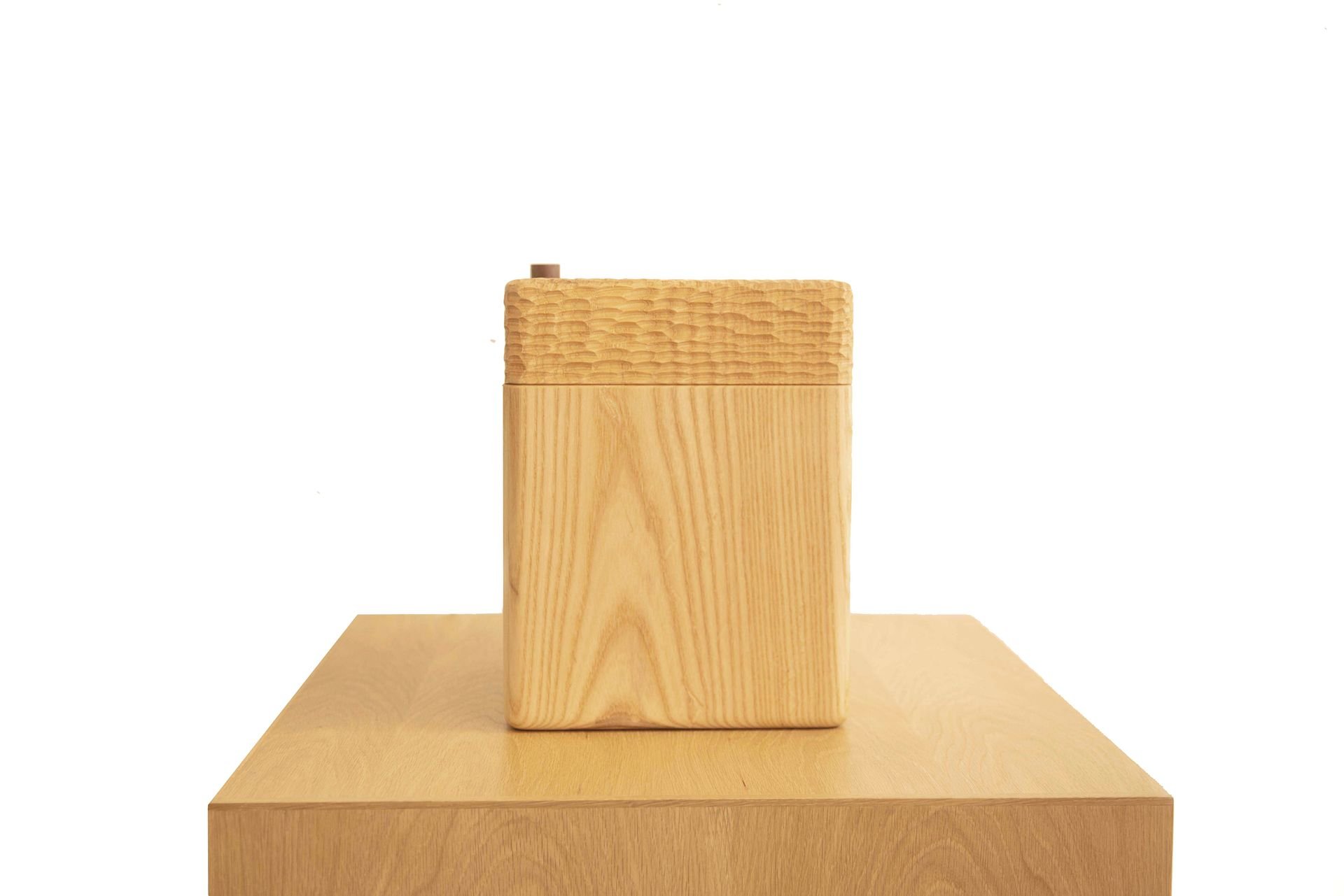 A wooden block sculpture on a wooden pedestal, with a plain white background.