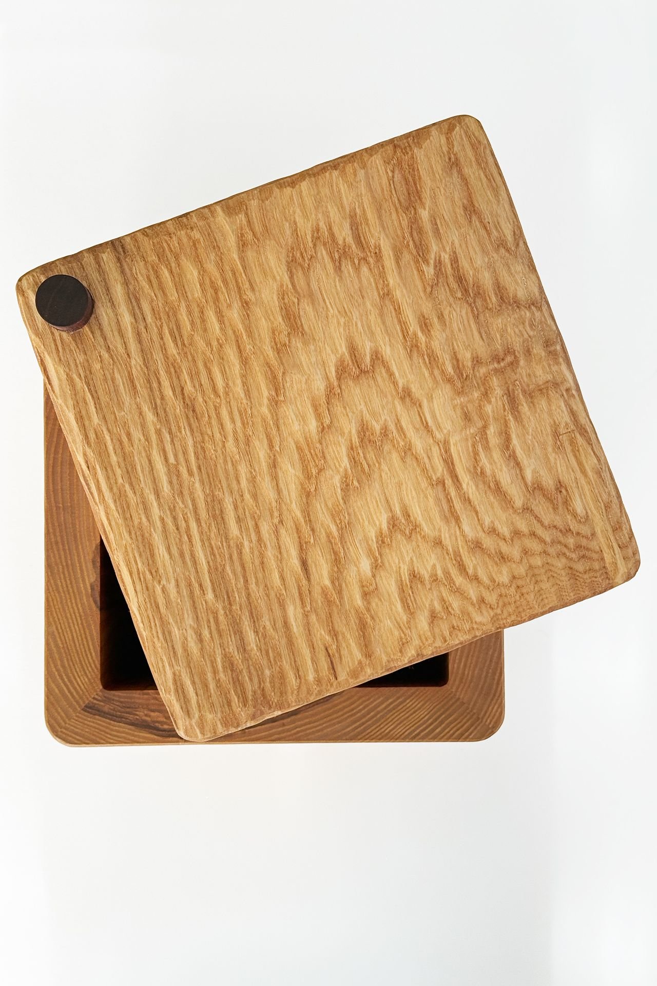 A close-up of a wooden stool with a square seat and slightly rounded edges, placed on a white surface.