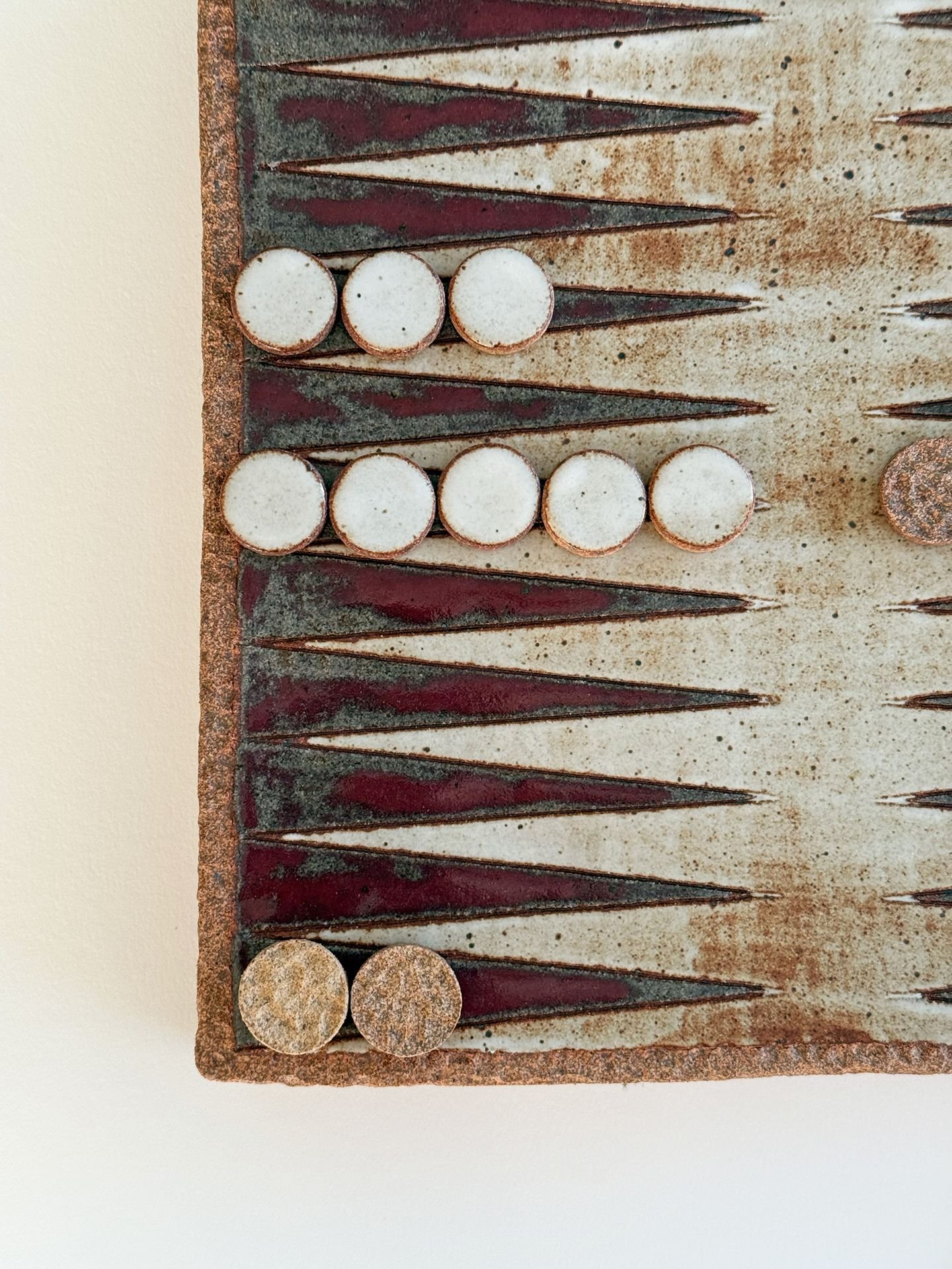 Close-up of a vintage backgammon game board with white and brown game pieces on a brown, worn board with carved dark triangles.