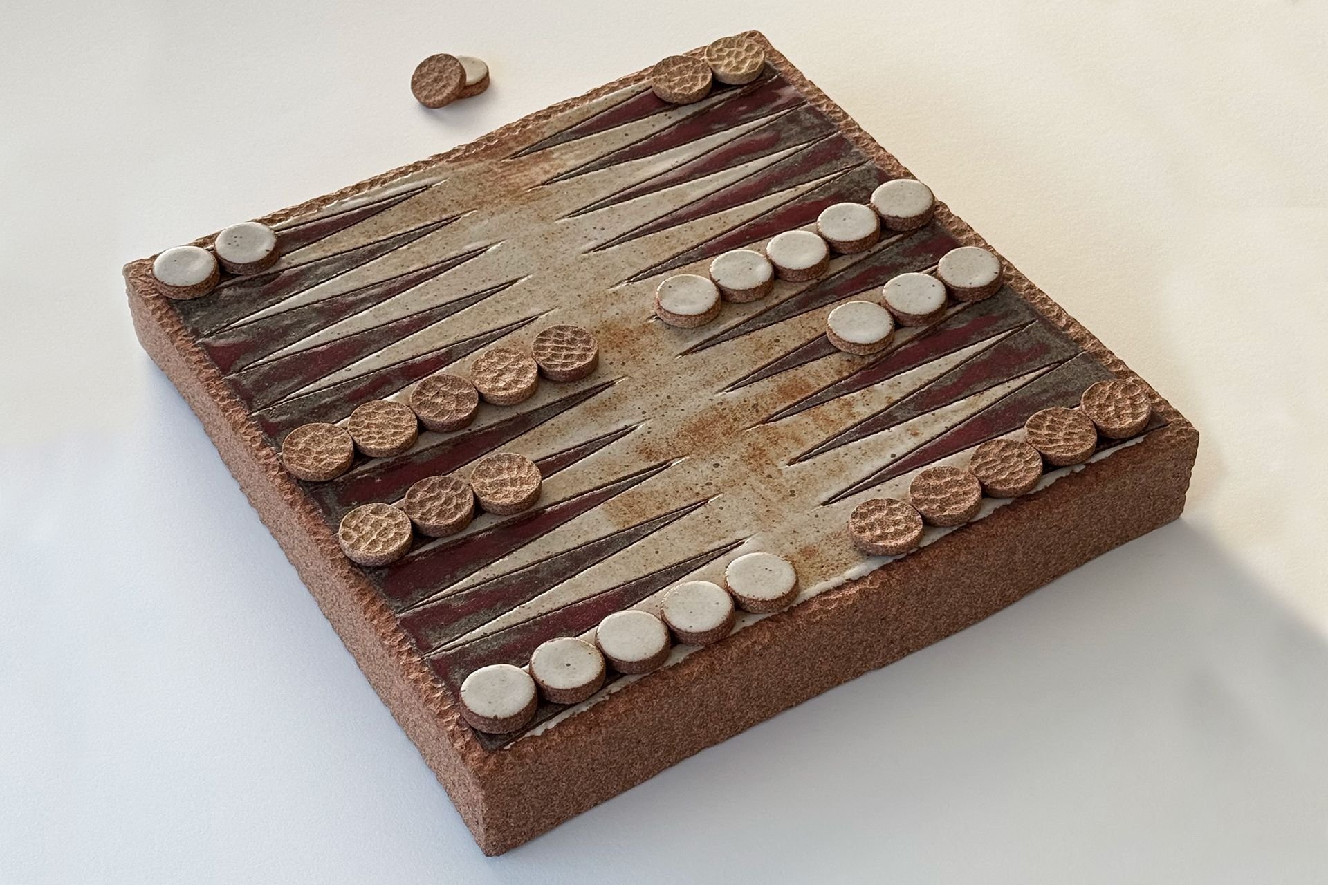 A close-up view of a chessboard with a checkered pattern, made of brown and beige tiles, placed on a white surface. There are no chess pieces visible.